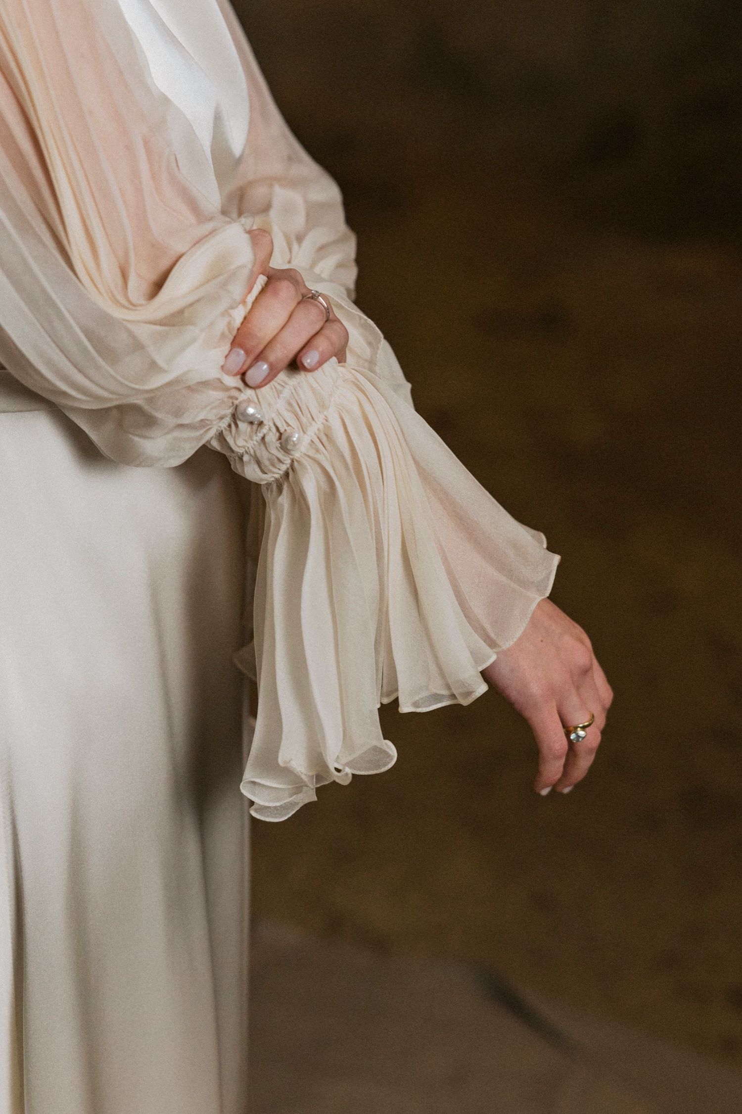 Close-up details of a delicate cream-colored silk dress with gathered fabric and ruffled sleeves.