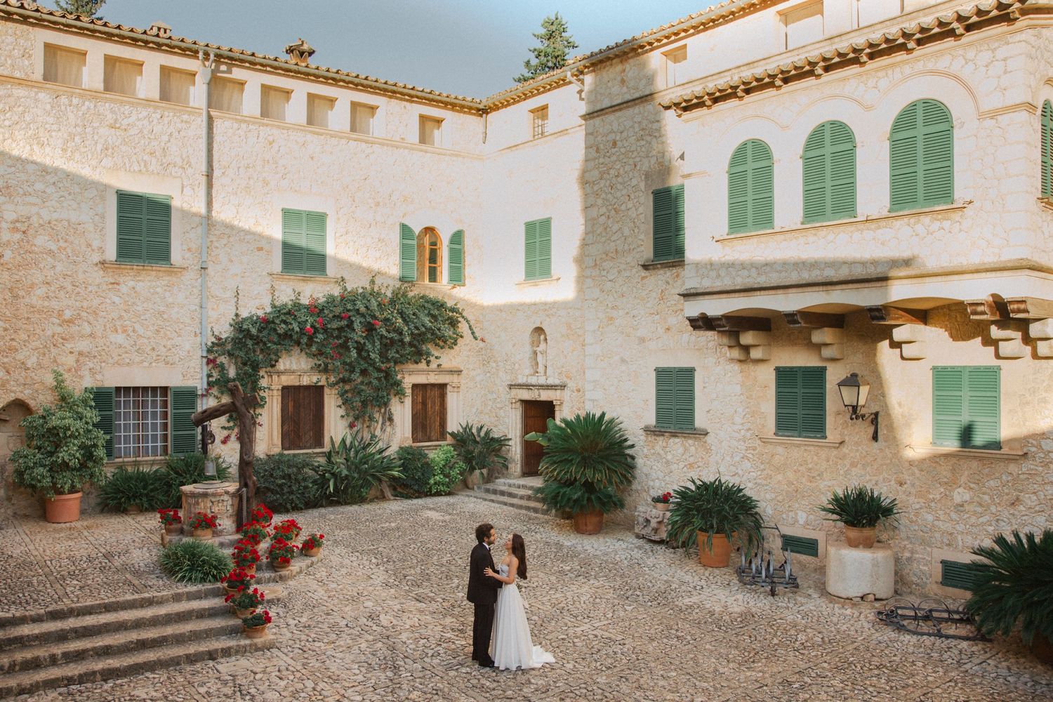 Mediterranean courtyard with white stone walls, green shutters, and terracotta roof tiles at a rustic Spanish villa.