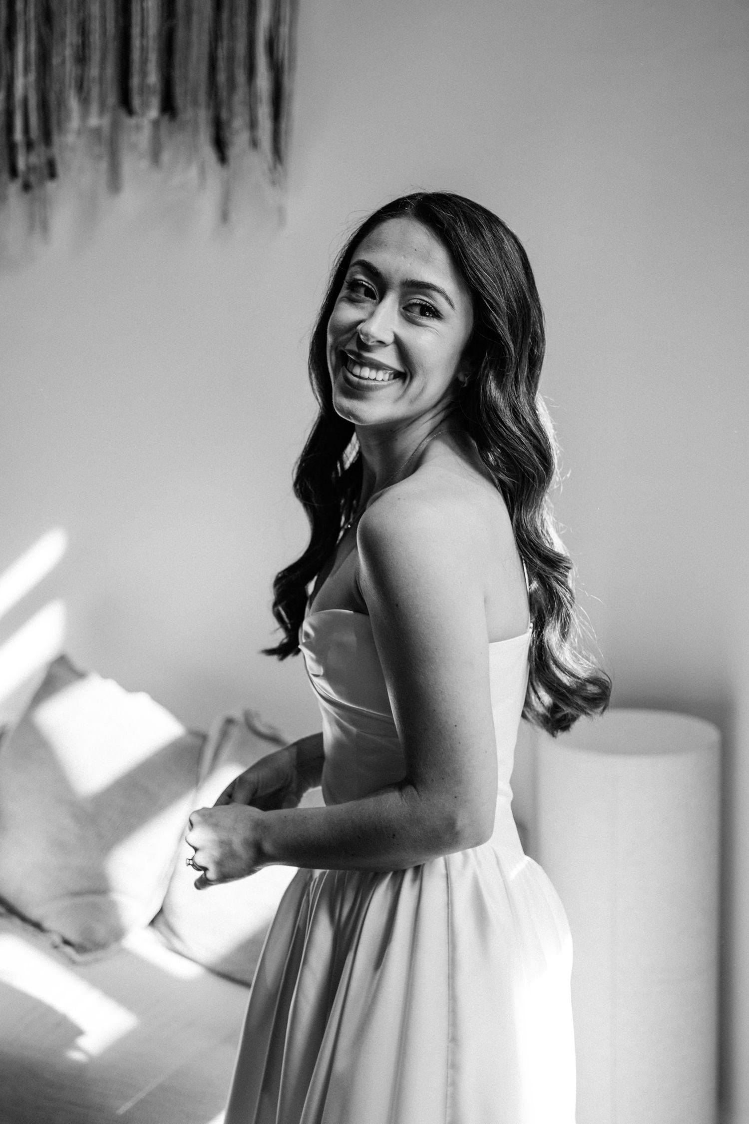 Black and white portrait of someone in a strapless white dress smiling joyfully while turning towards the camera.