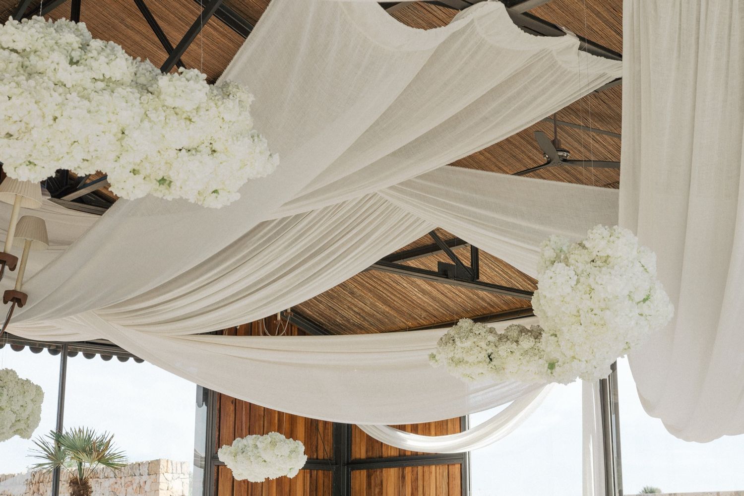 Elegant wedding venue ceiling decorated with white draped fabric and white hydrangea floral arrangements.