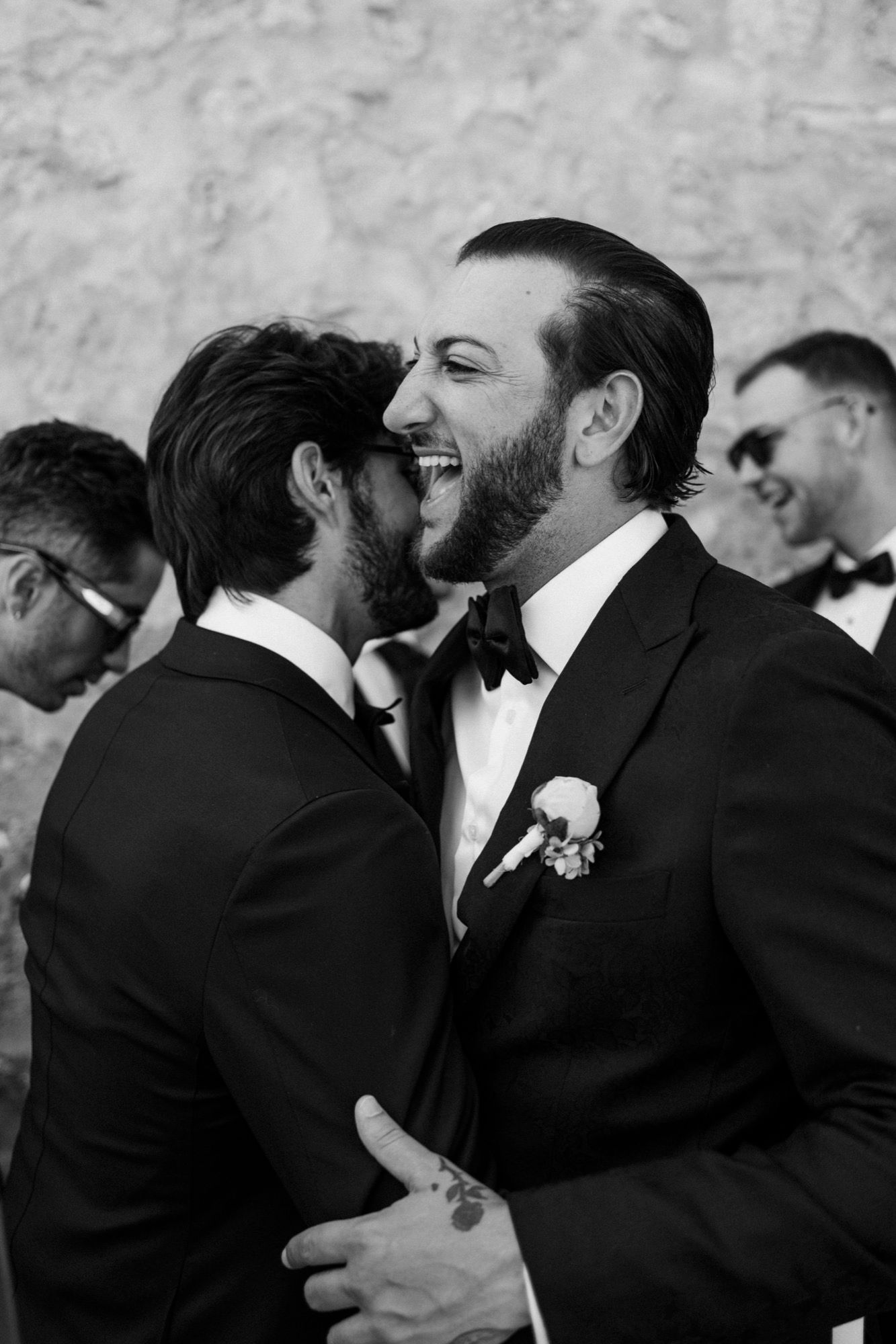 Groomsmen share emotional embraces in black and white formal attire.