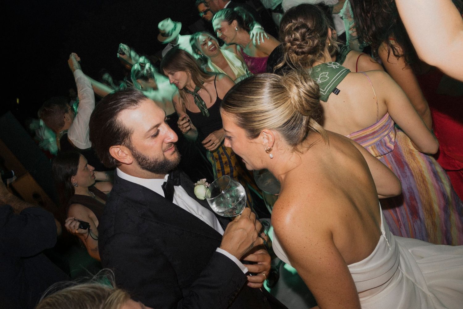 Couple surrounded by wedding guests share intimate moment during lively dance floor celebration.