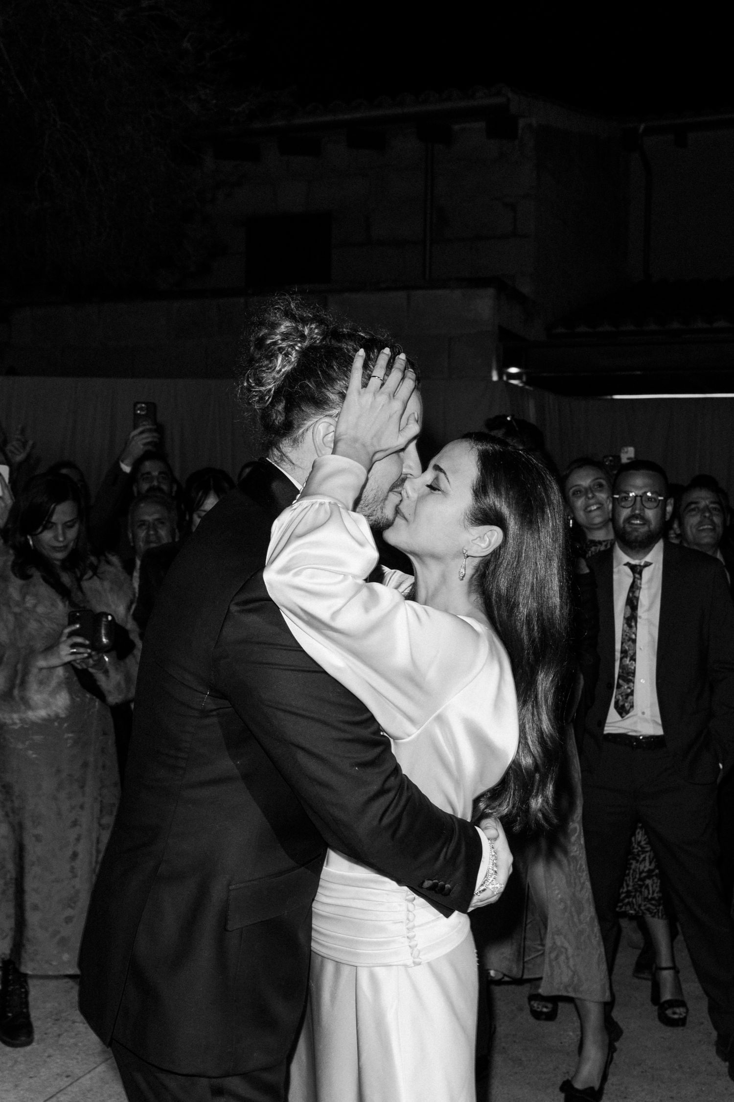 A couple shares a passionate kiss during their wedding reception surrounded by guests.