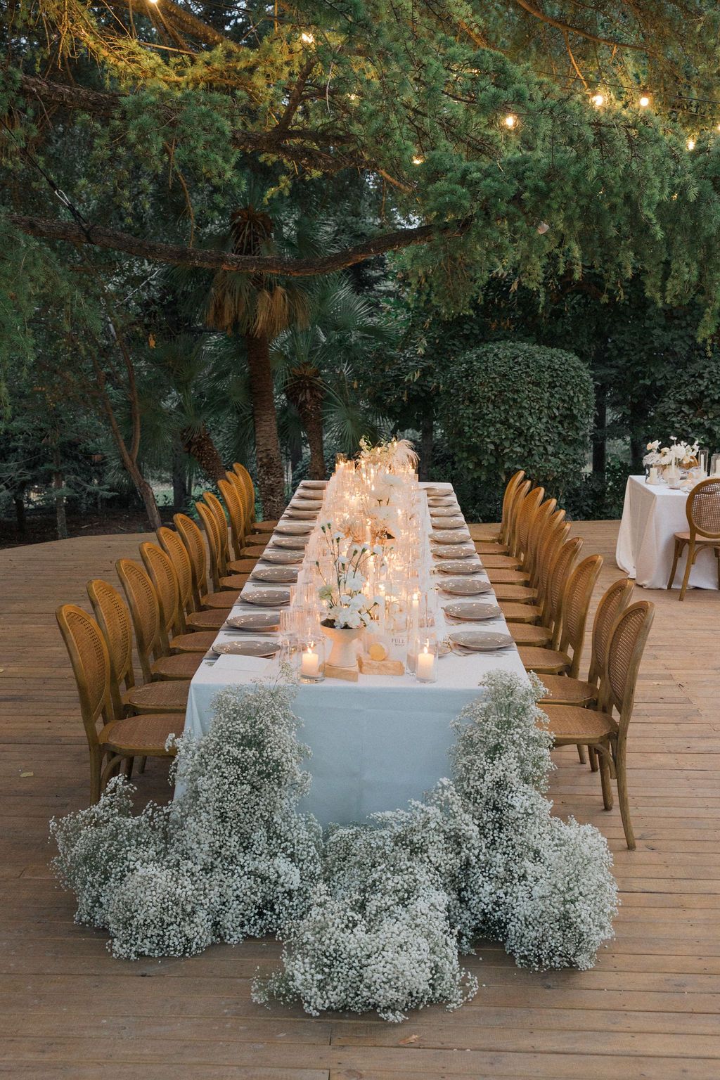 Wedding reception tables decorated with baby's breath flowers and white linens under string lights.
