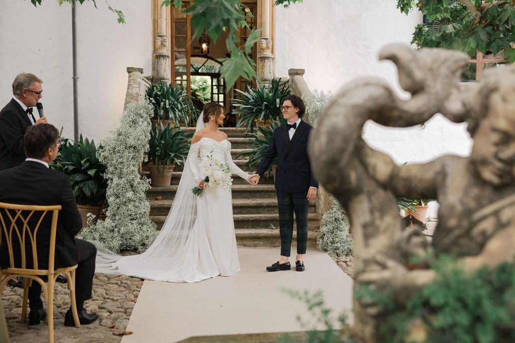 A wedding ceremony in a courtyard with decorative stone elements and greenery.