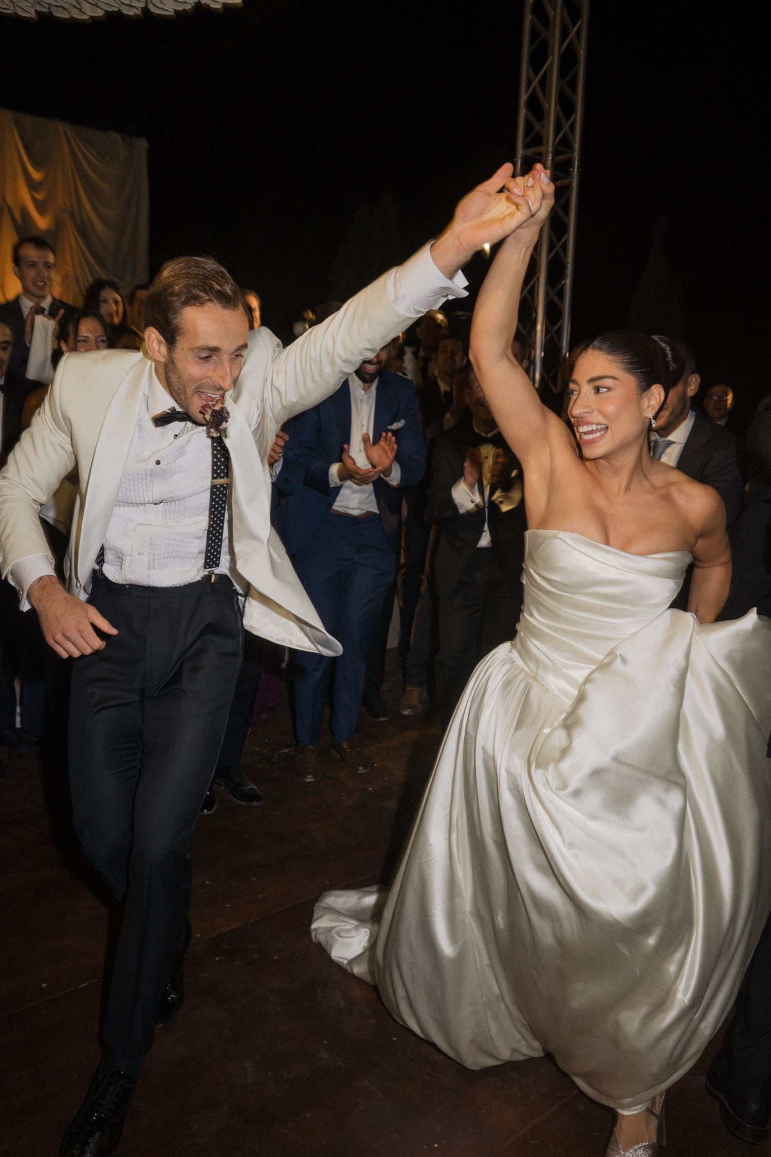 A couple dances joyfully at their wedding reception, with the bride in a white strapless gown and groom in formal attire.