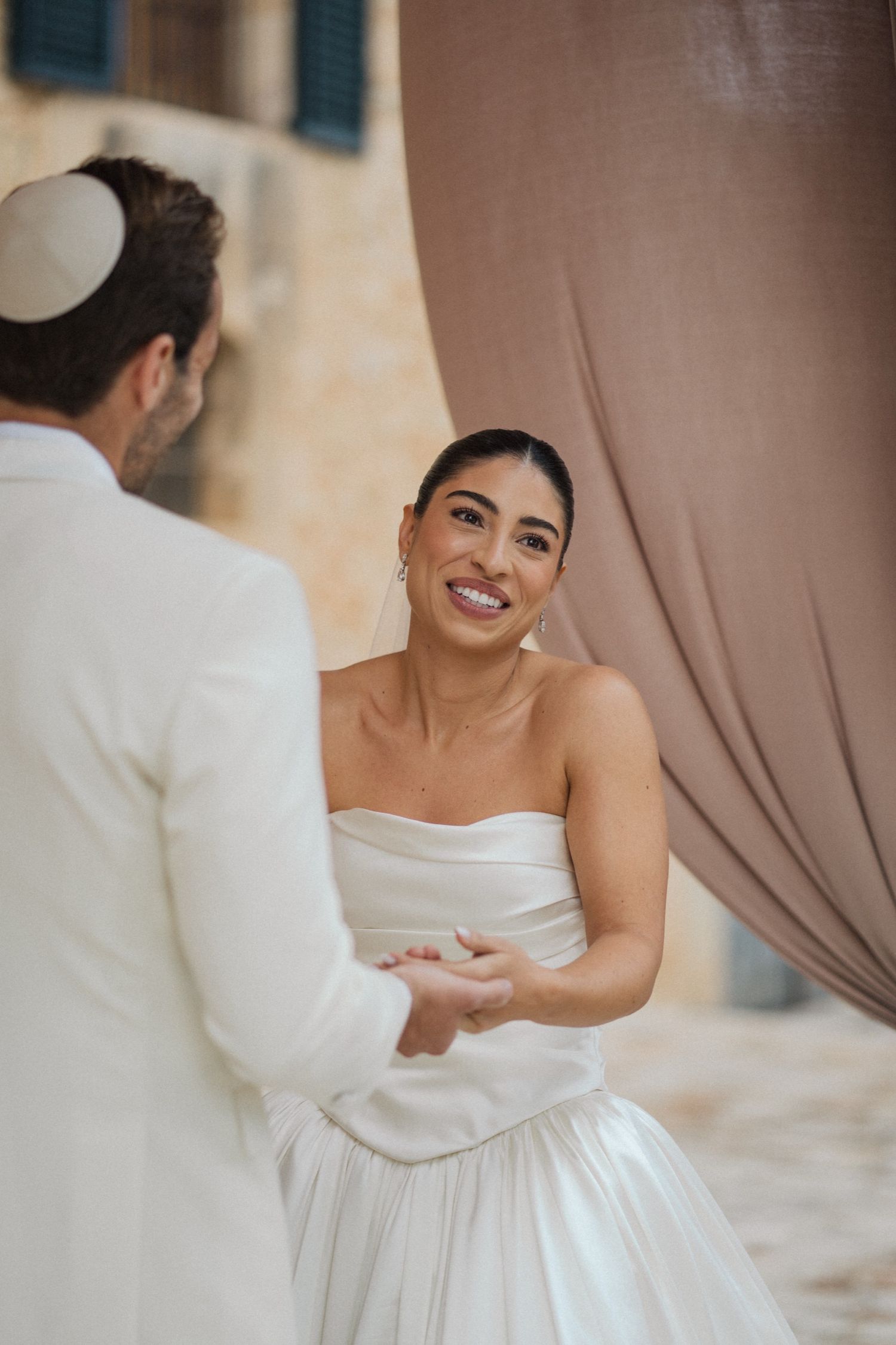 A couple in white wedding attire share a joyful moment during their ceremony.