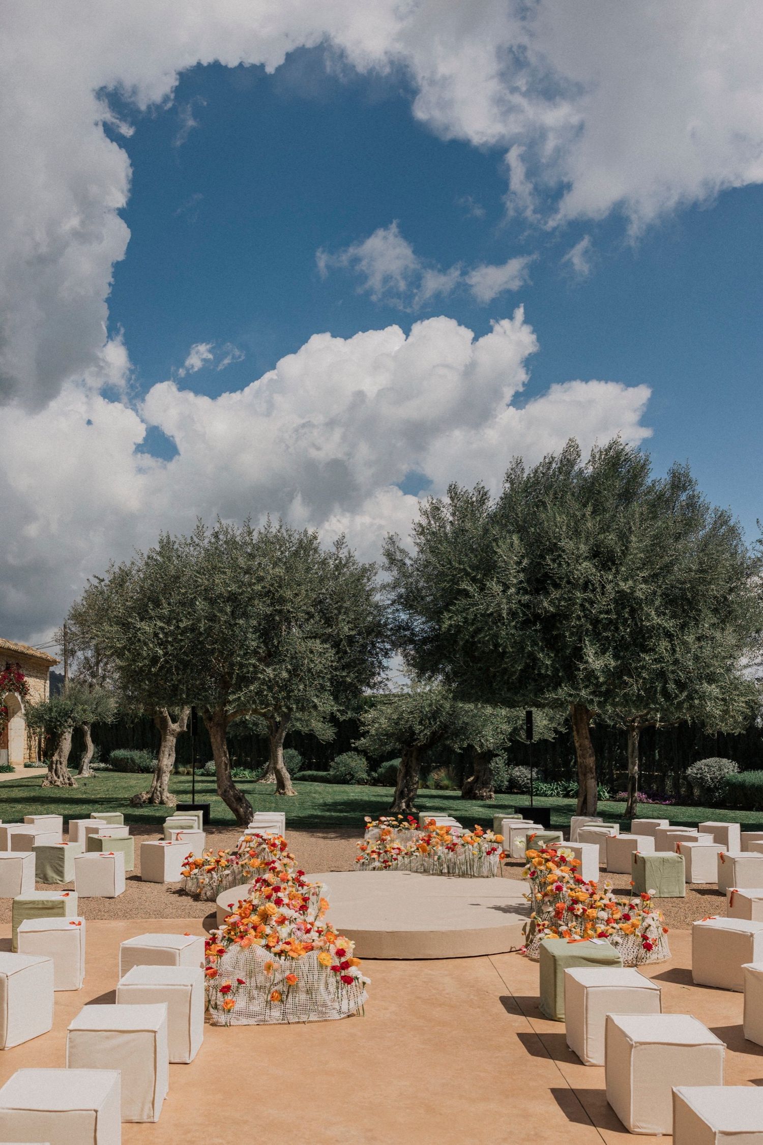 Modern outdoor event venue with white stone benches and orange floral arrangements under a bright blue sky.