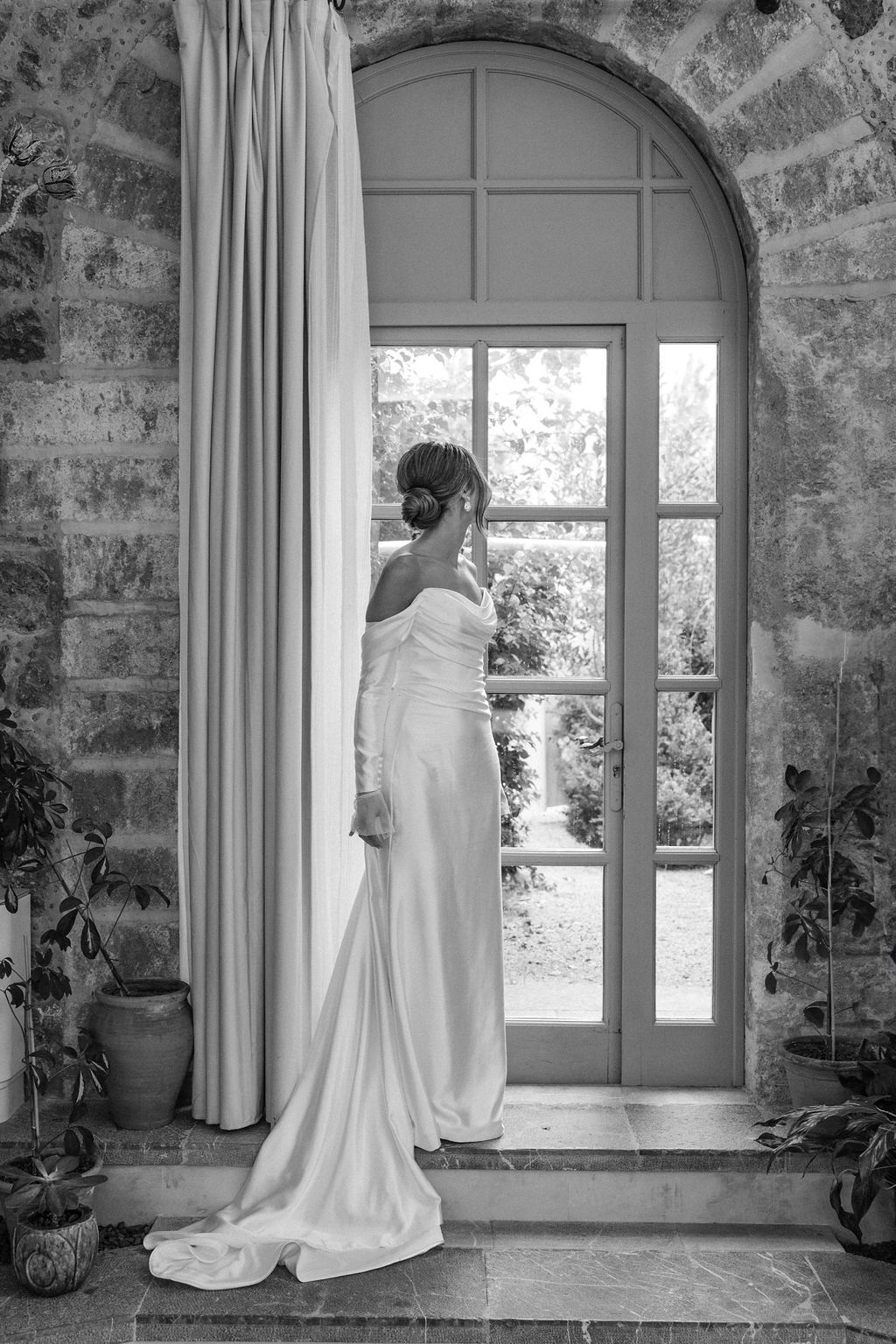 Elegant white wedding gown displayed in front of an arched window in a stone room.