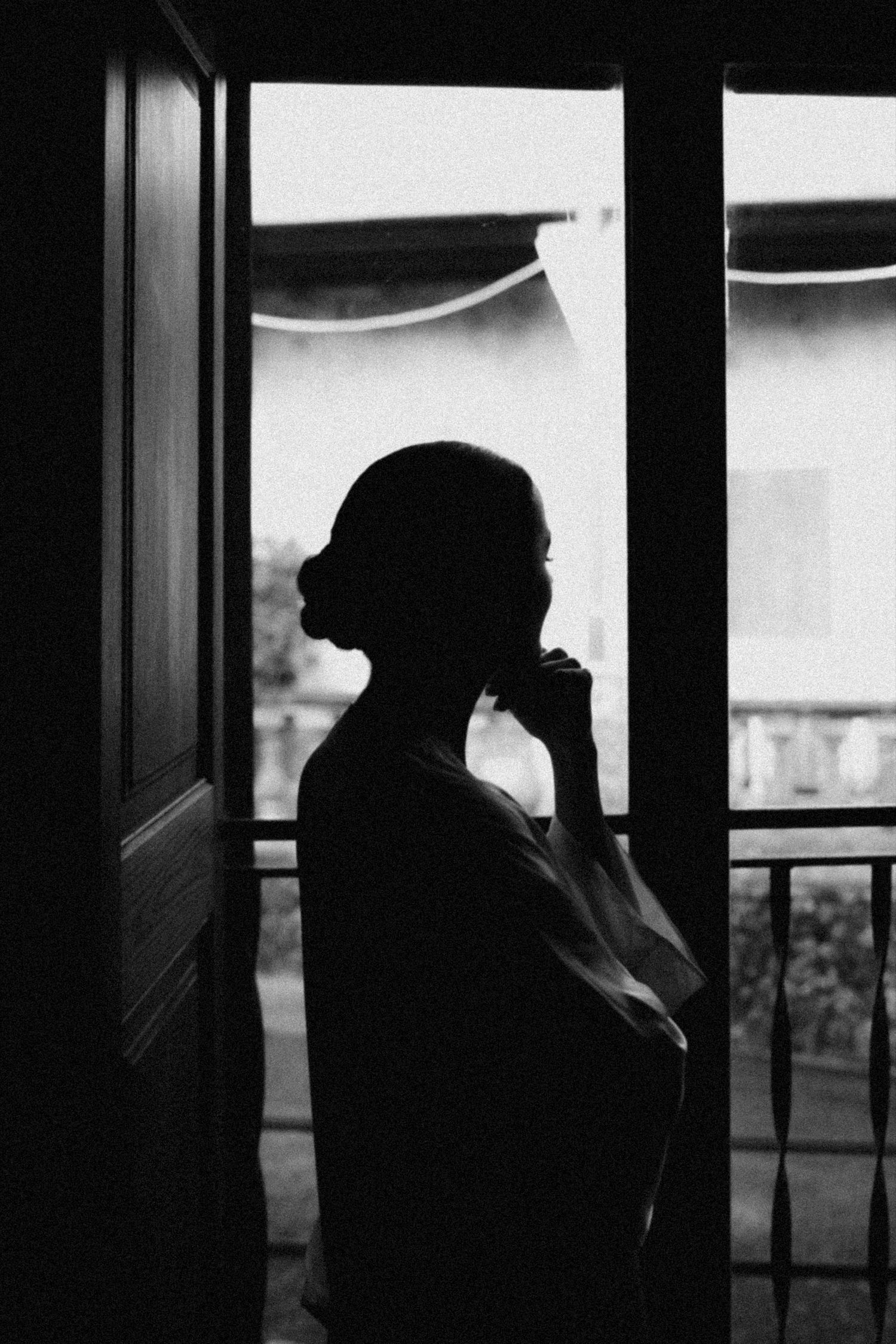 Silhouetted figure by window creates dramatic contrast in black and white photography.