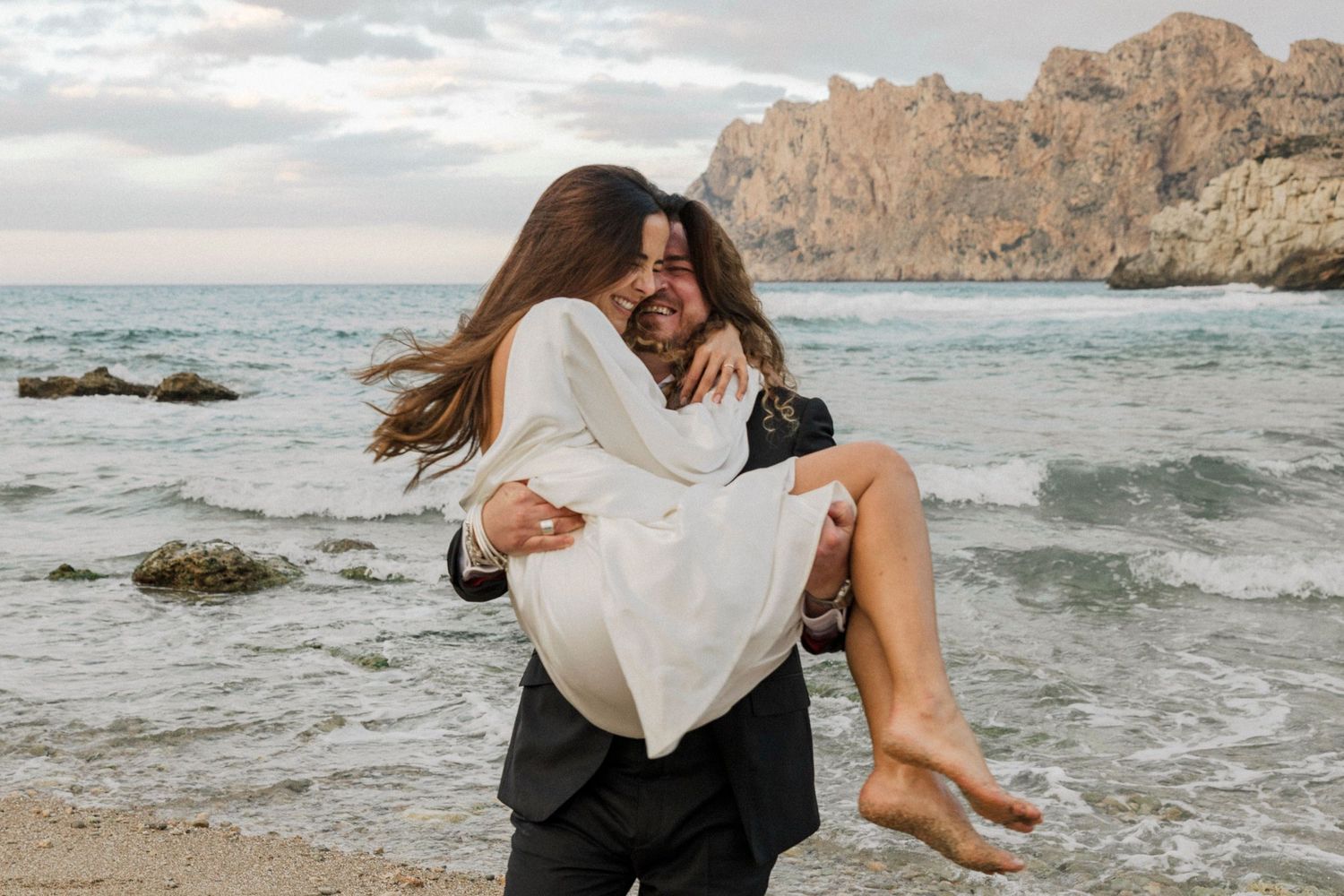 Romantic beach scene with couple in playful lift pose against ocean backdrop.