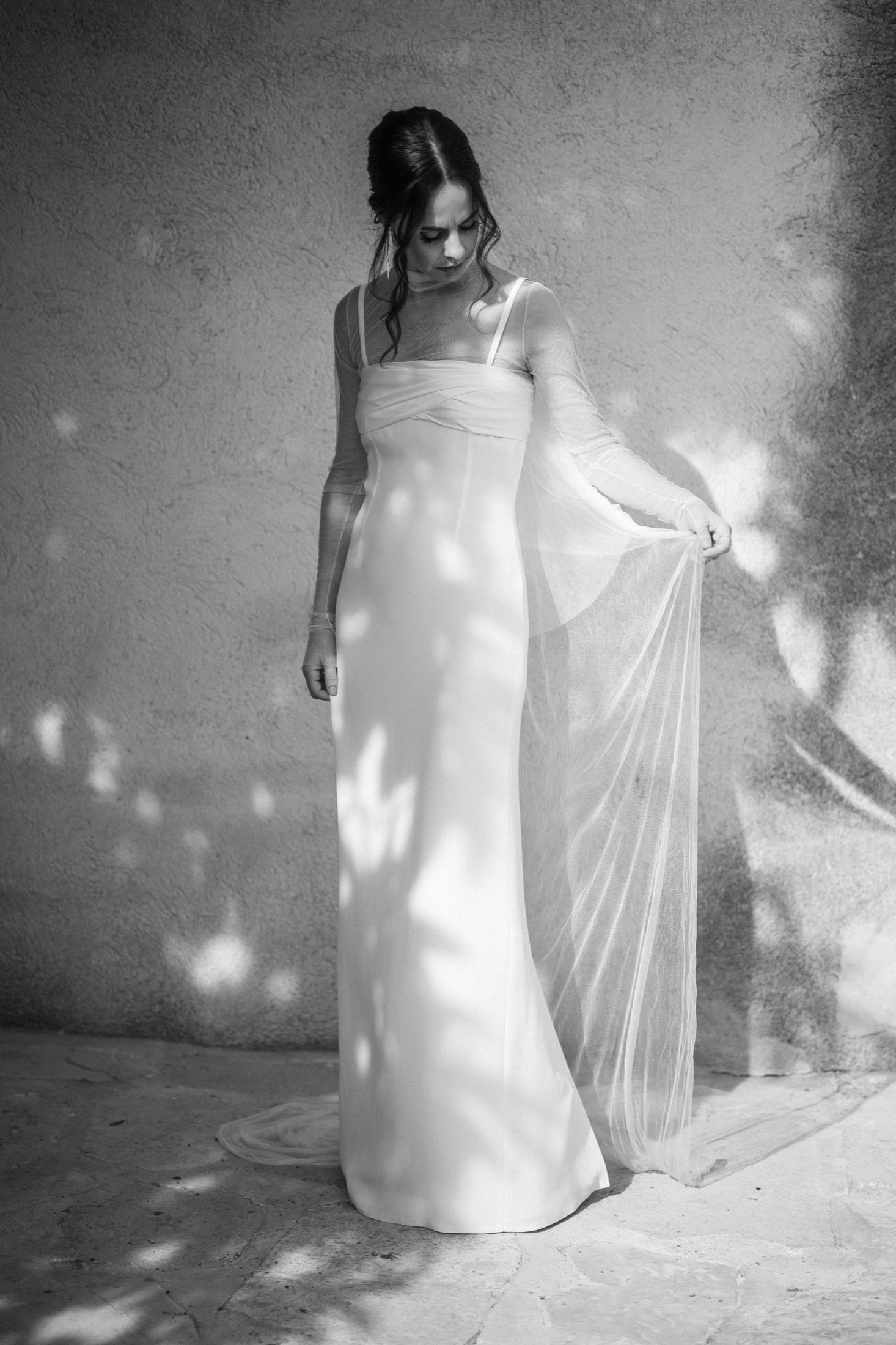 A series of black and white photos showing a figure in a flowing white dress creating ethereal movement against a textured wall.