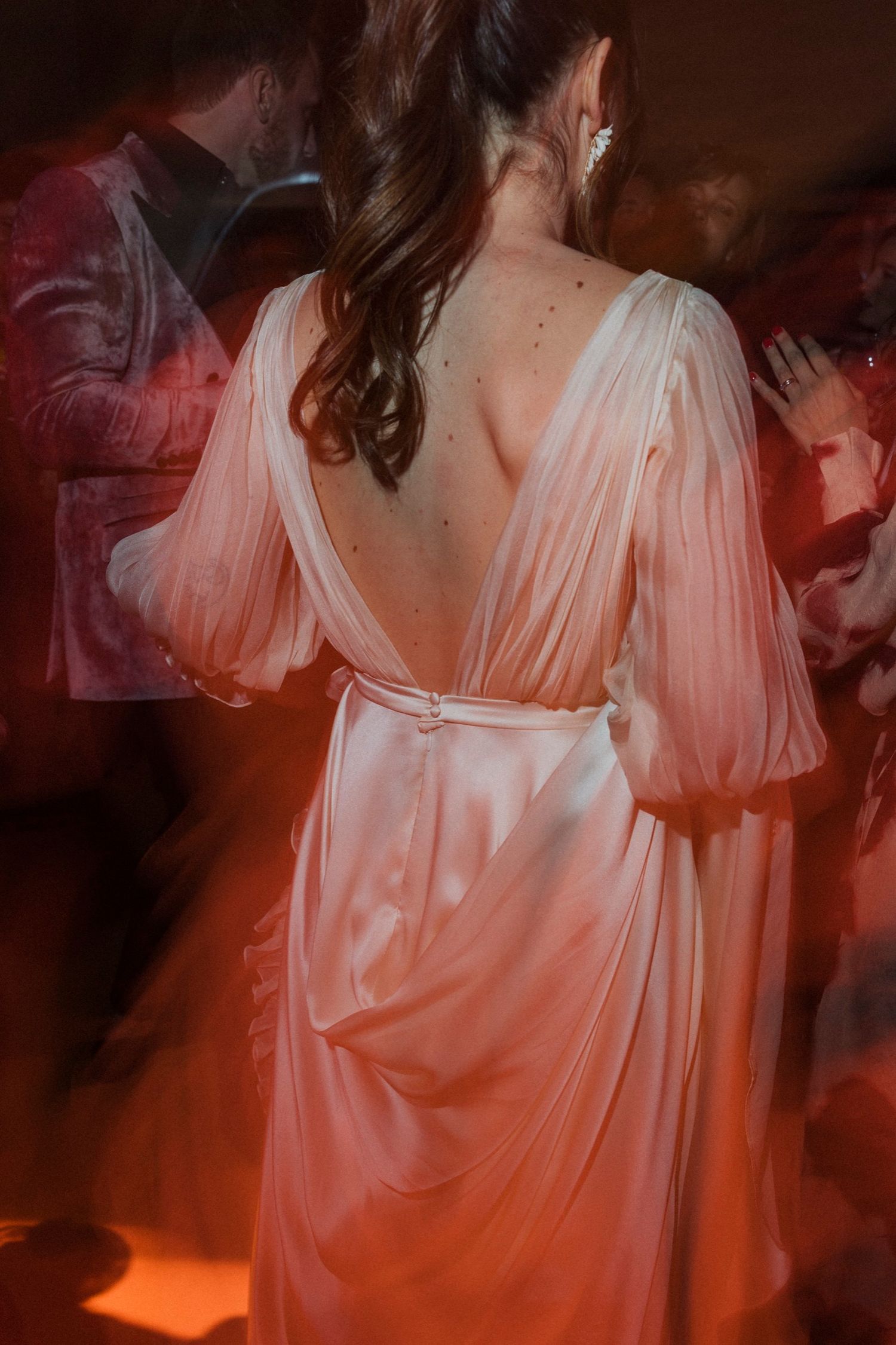 Back view of an elegant pink silk dress with billowing sleeves and open back design in dramatic lighting.