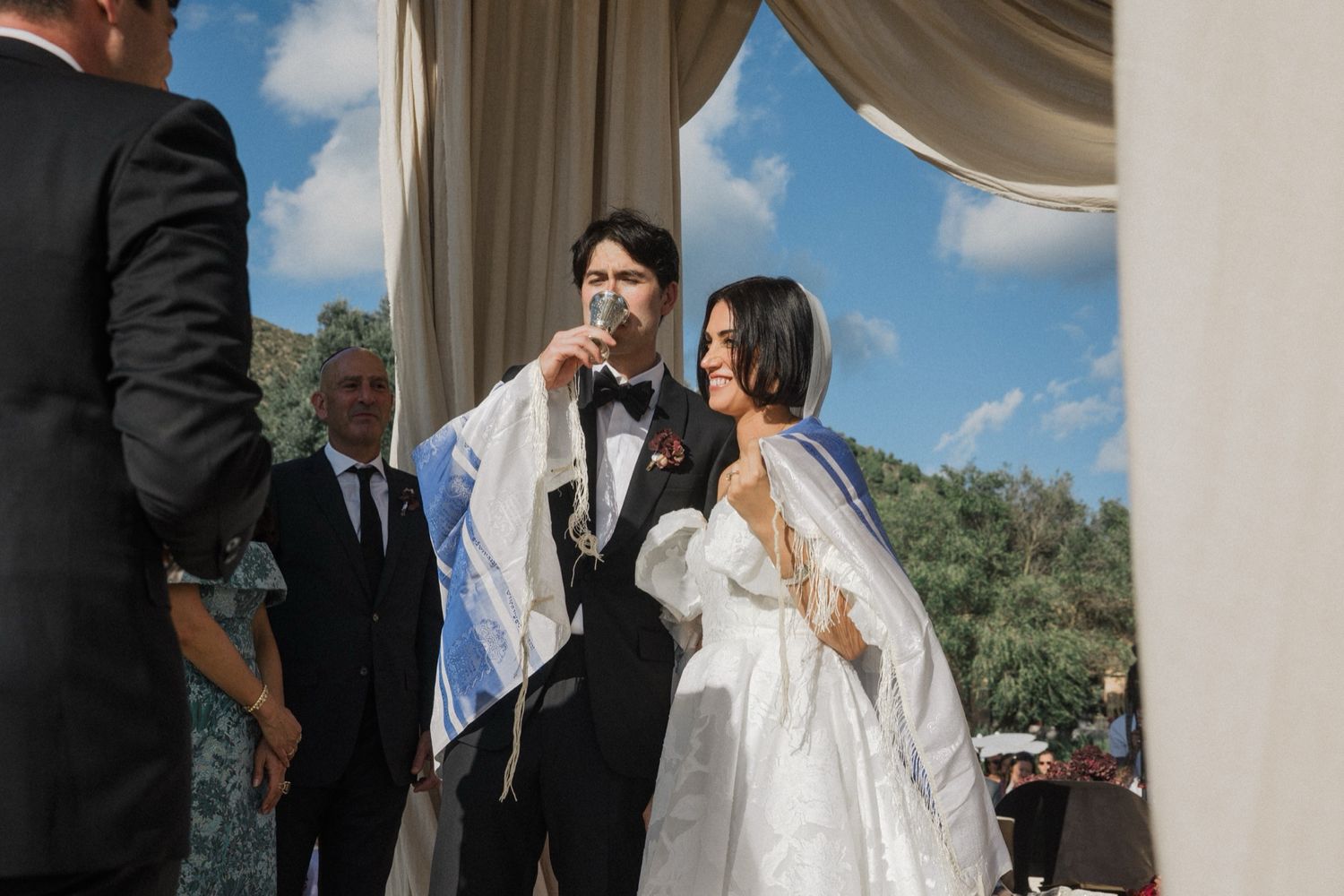 Bride and groom share a romantic moment during their outdoor wedding ceremony under blue skies.