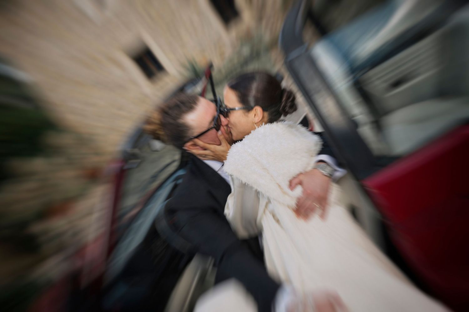 Artistic blurred wedding photo capturing an intimate moment between newlyweds near a red car.