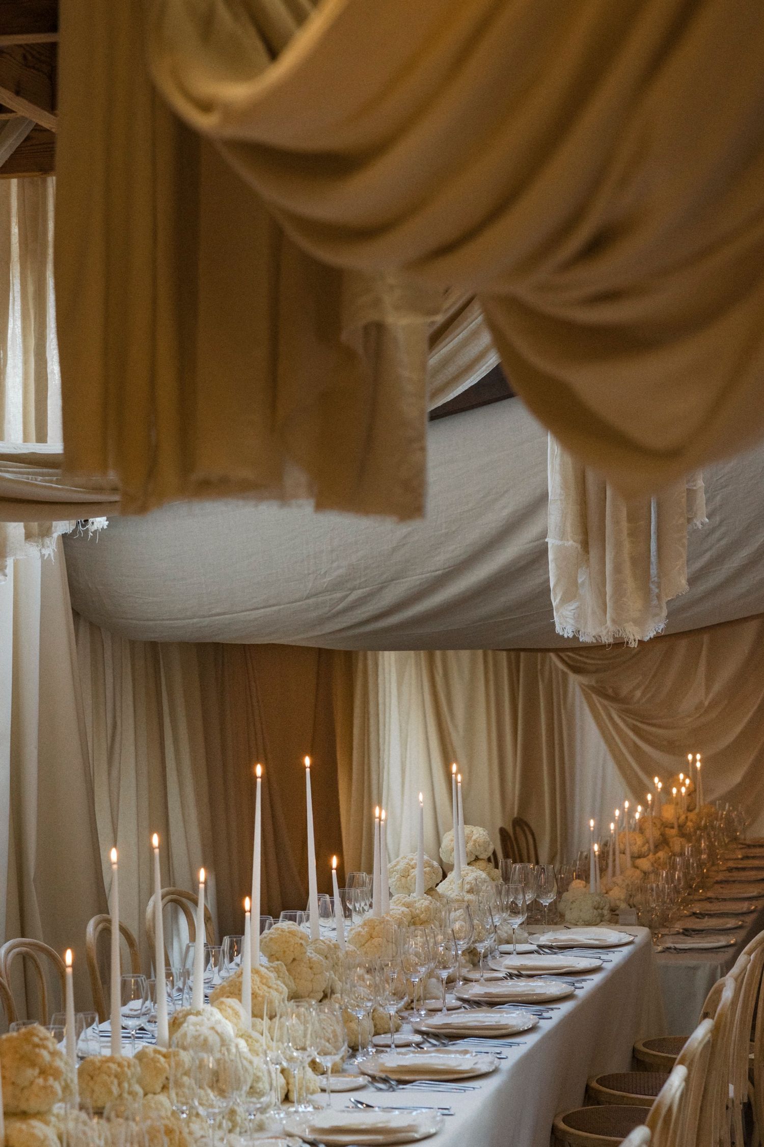 Elegant wedding reception table setting with white draping, candlelight, and floral centerpieces running down a long table.