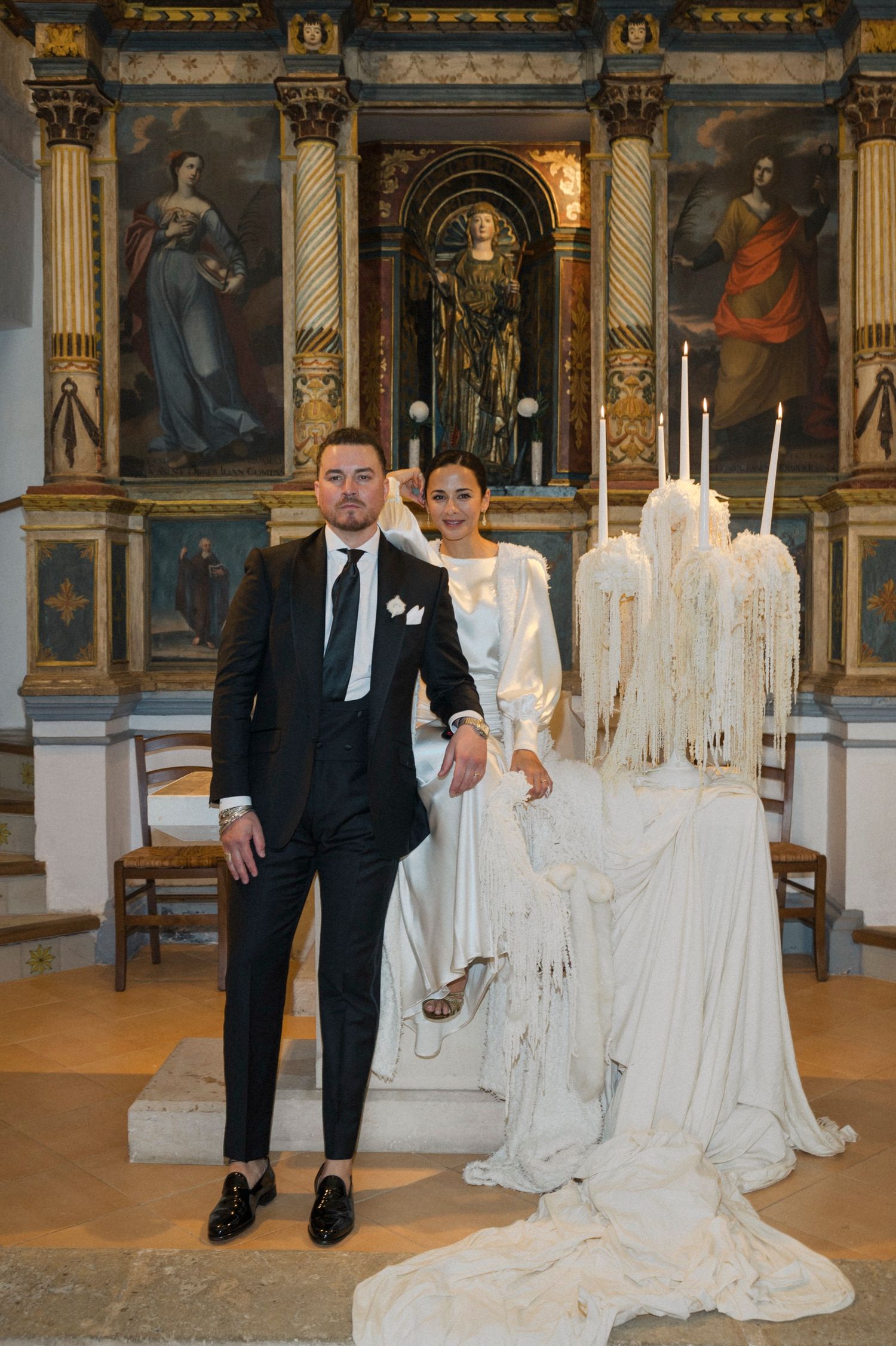 Couple posing in formal attire next to white draped fabric installations in a church.