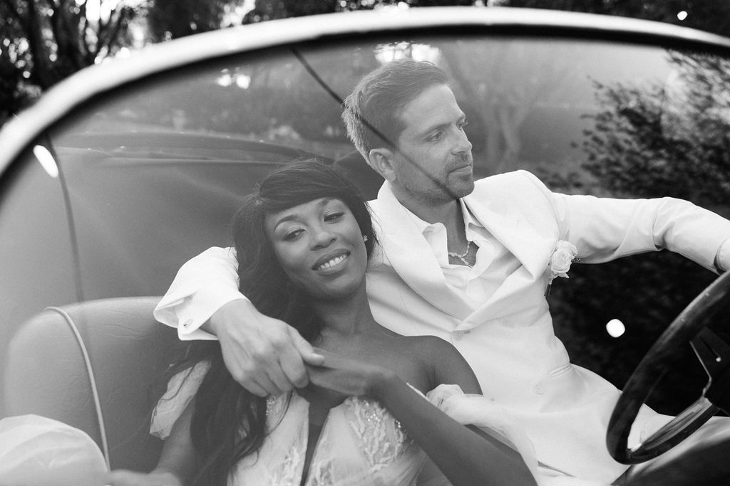 Romantic couple sharing intimate moments in a classic convertible car during a photoshoot.