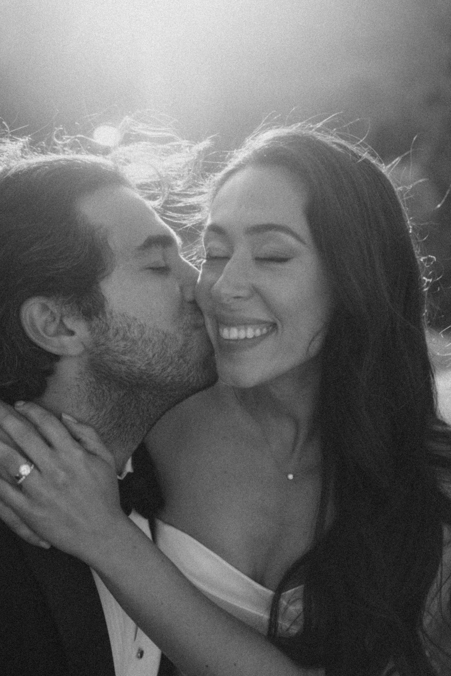 A romantic black and white photo of a couple sharing an intimate moment with sunlight creating a dreamy backlit effect.
