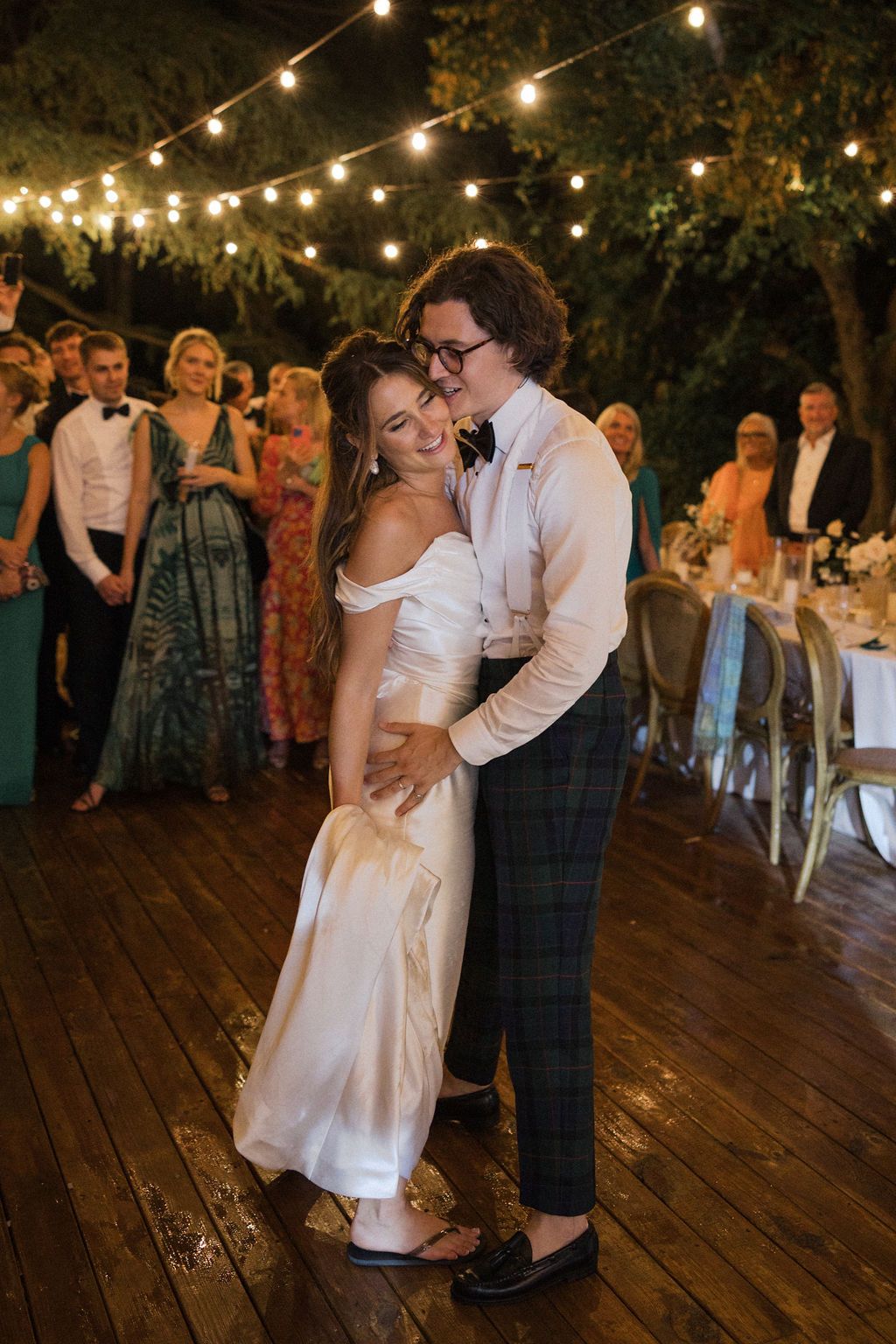 Couple sharing a romantic dance moment on wooden deck under twinkling lights.