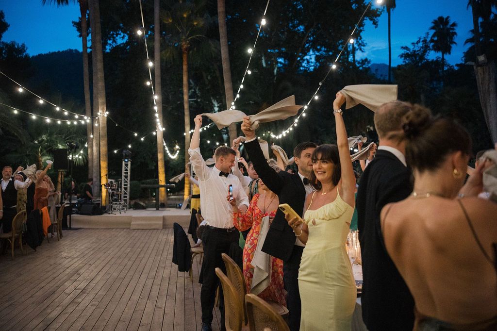 Wedding guests dancing under string lights at an outdoor evening reception celebration.