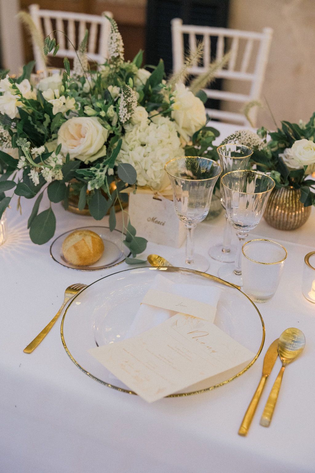White and gold wedding table setting with floral centerpieces and elegant place settings.