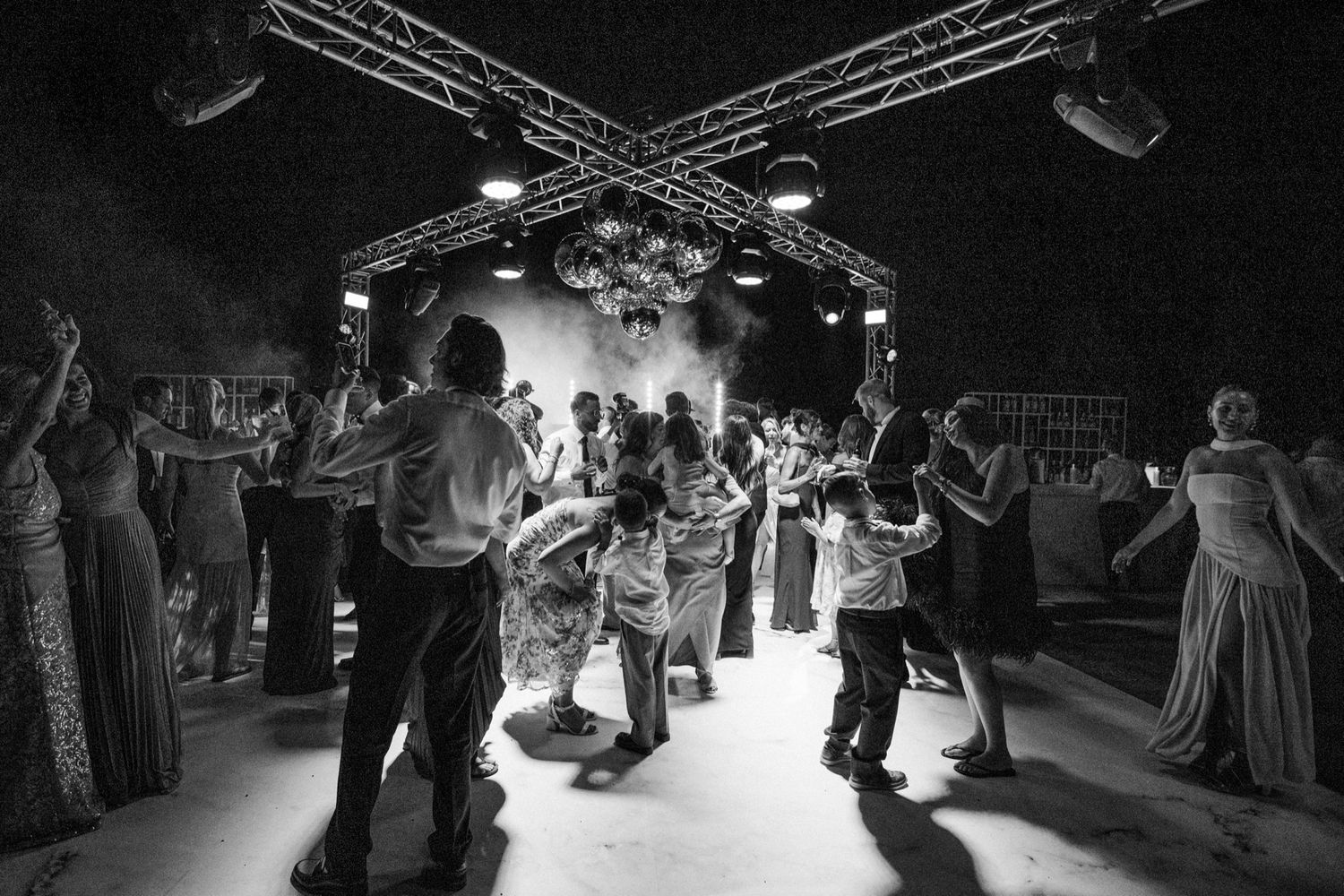 Black and white photo shows couples dancing under stage lighting at formal event.