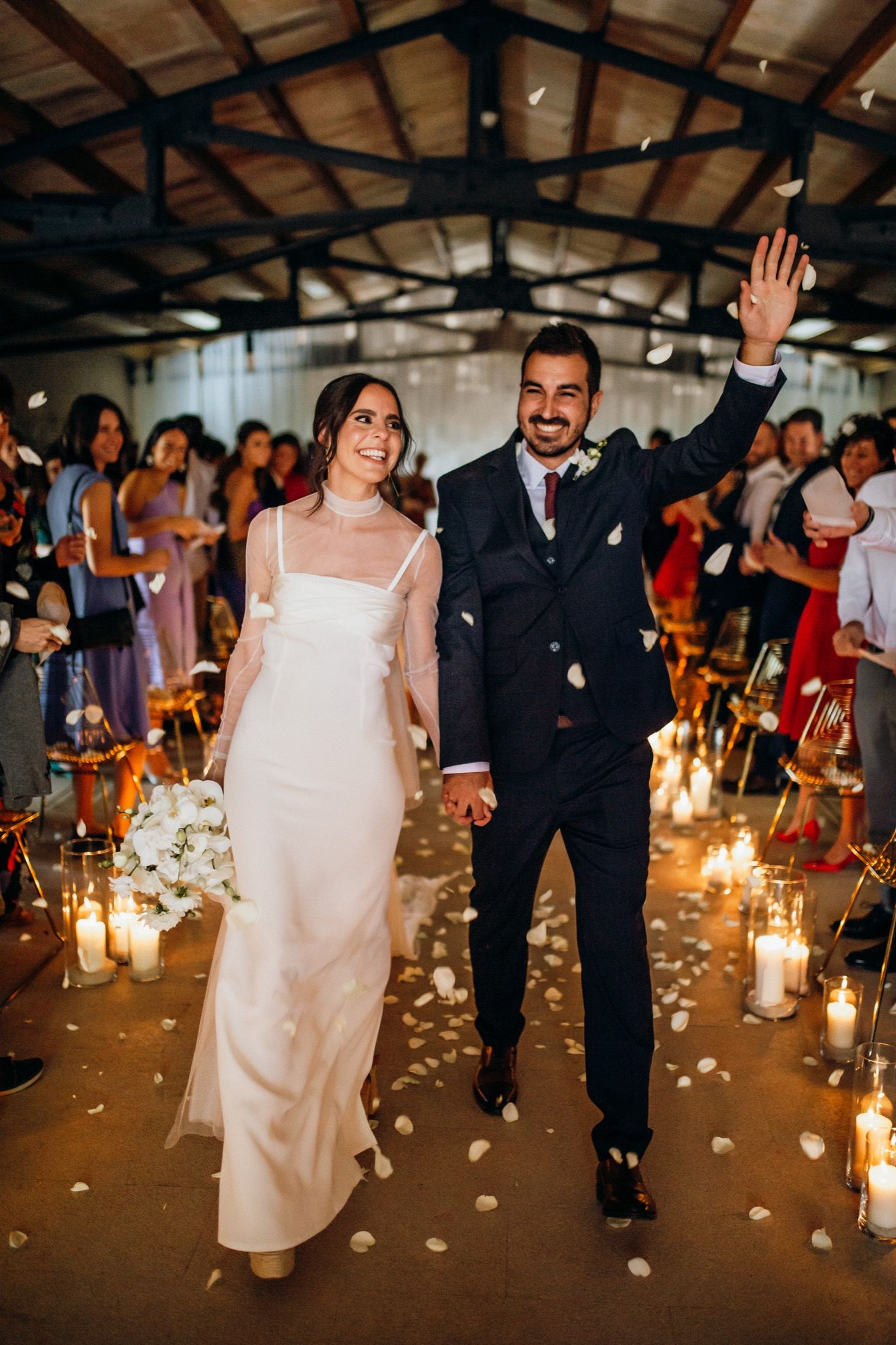 A couple walks down a candlelit aisle decorated with rose petals during an indoor wedding reception.