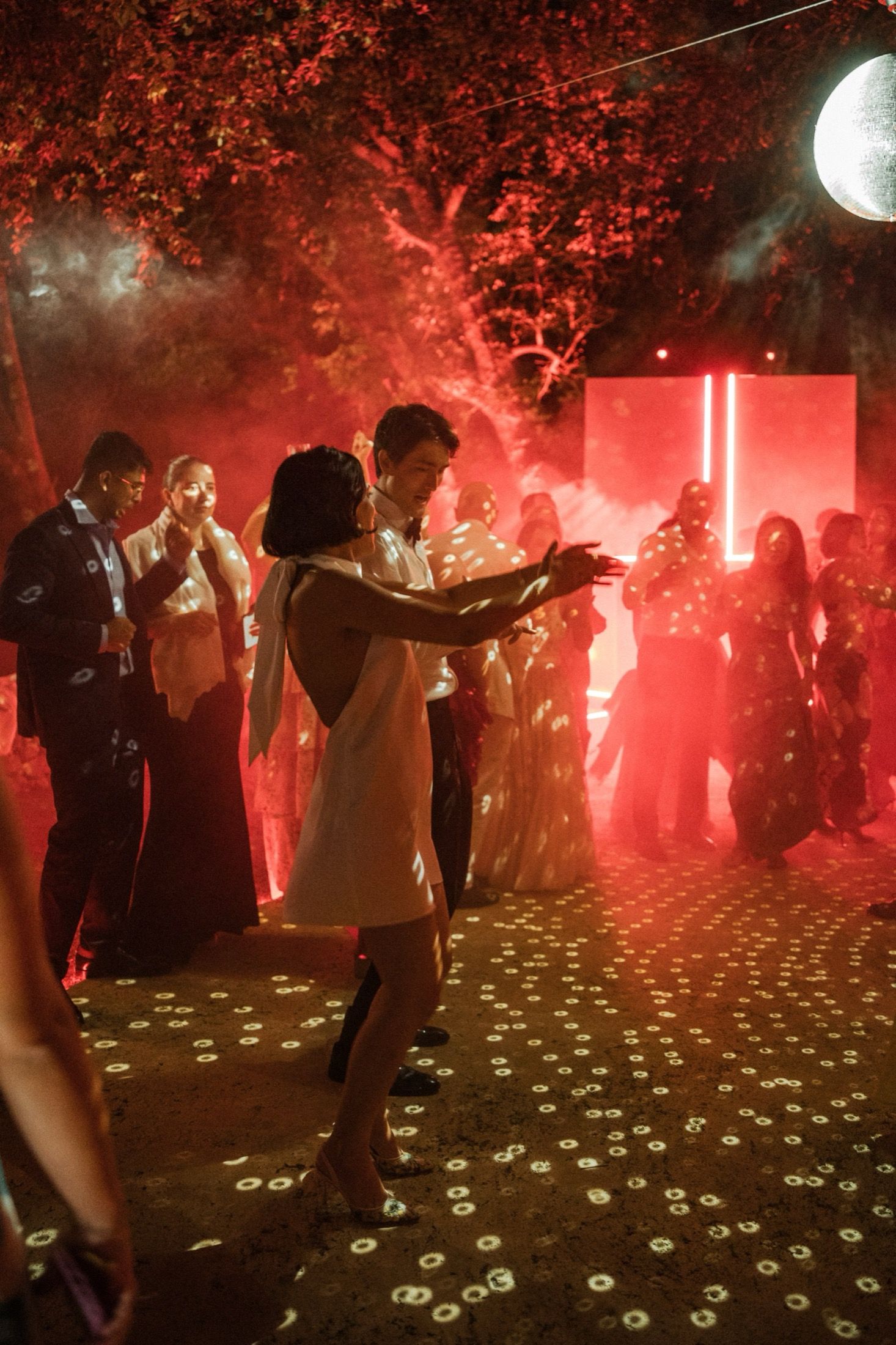 Dancers move on an illuminated dance floor filled with red smoke and bright flares during a nightclub party.