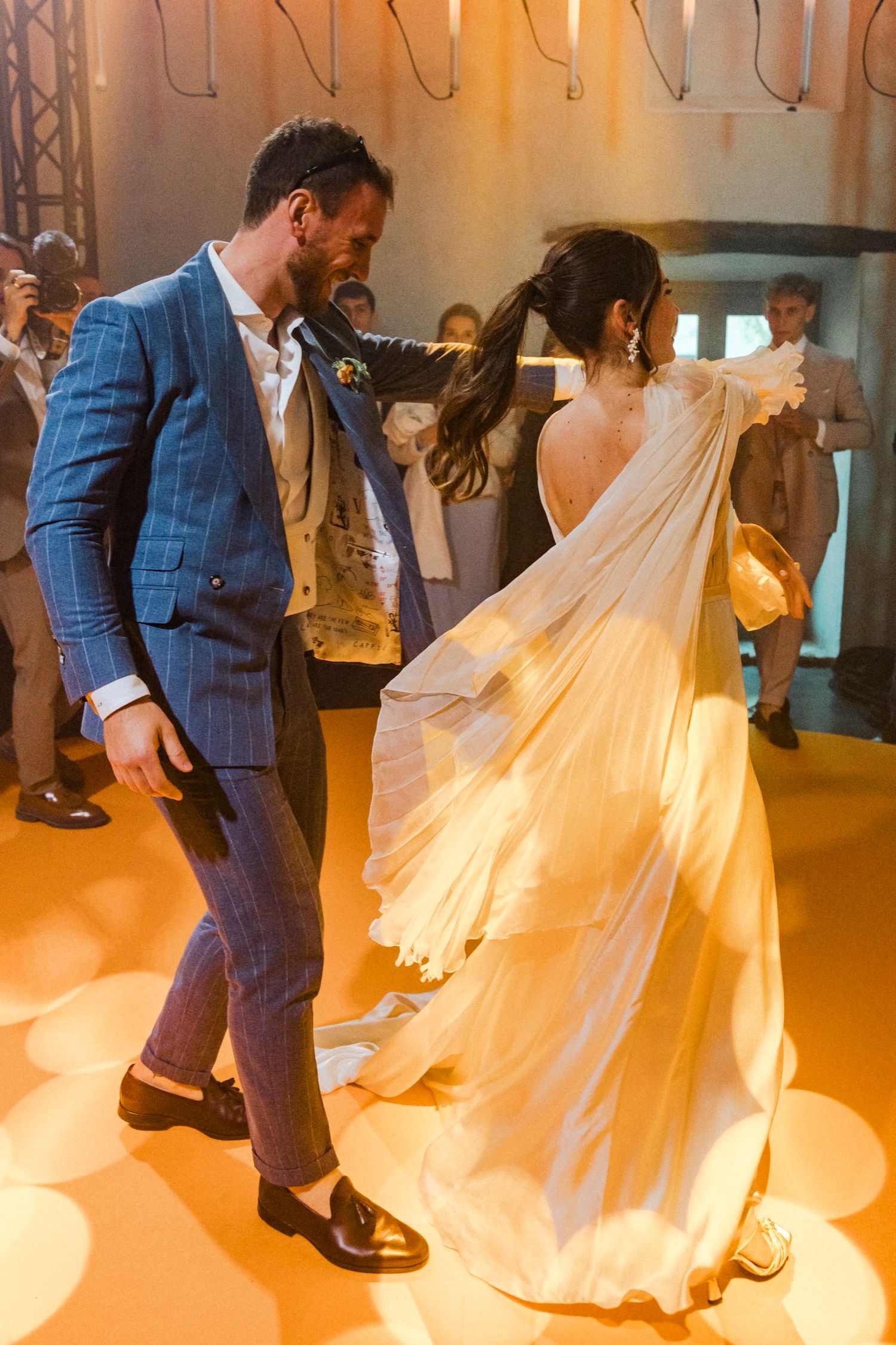 Newlyweds perform their first dance in a warm-lit venue as the bride's white dress twirls elegantly around them.