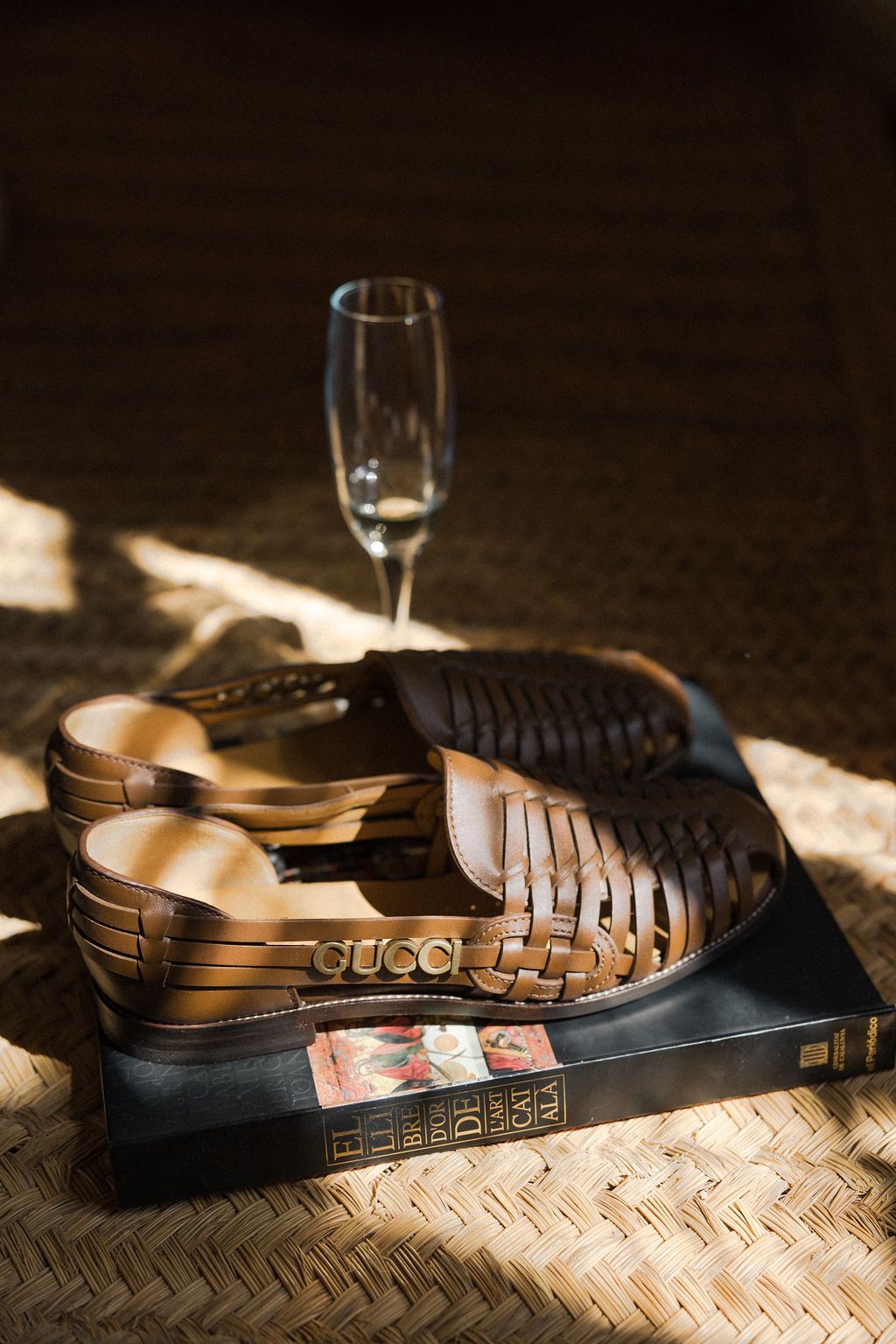 Designer leather sandals casting dramatic shadows on a textured surface.