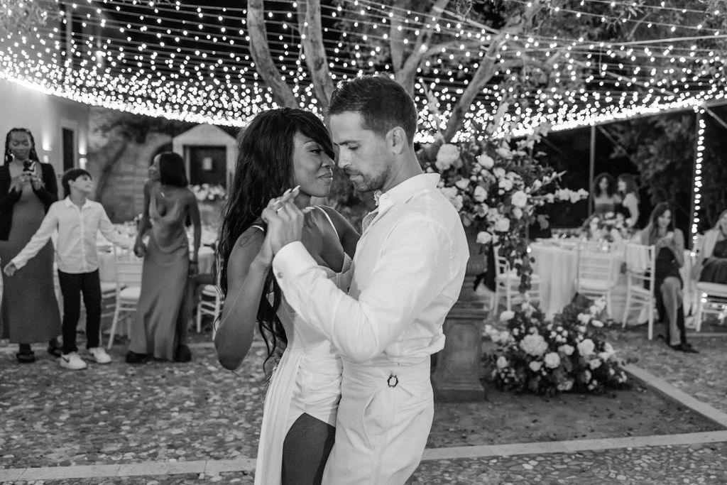 A couple shares a romantic dance moment under twinkling fairy lights at an outdoor reception.
