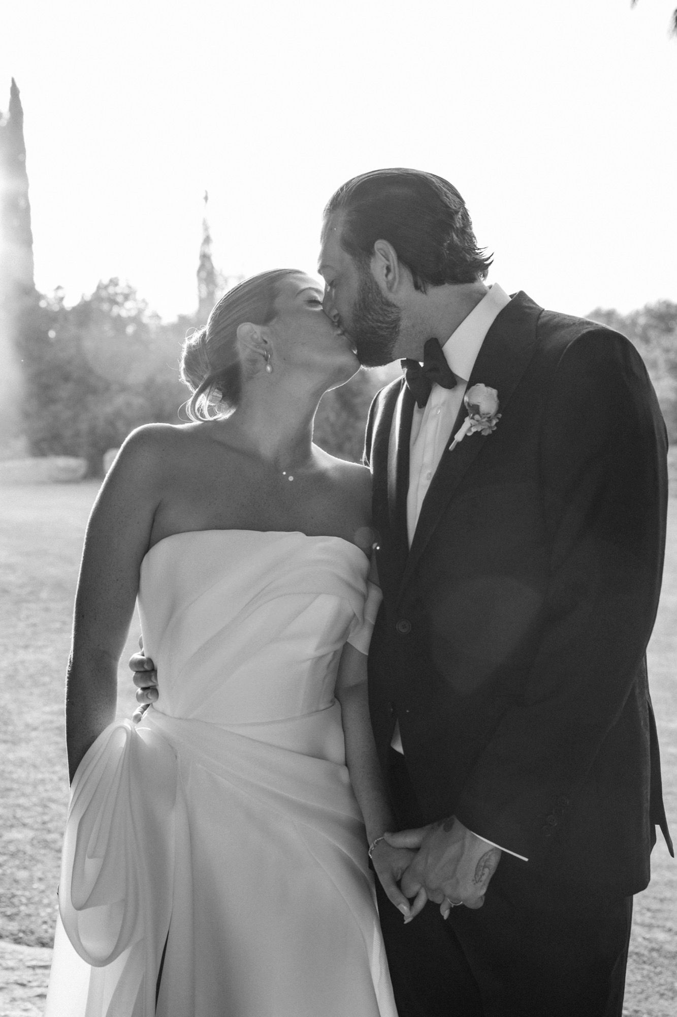 A romantic black and white wedding photo of a couple sharing a tender kiss outdoors.