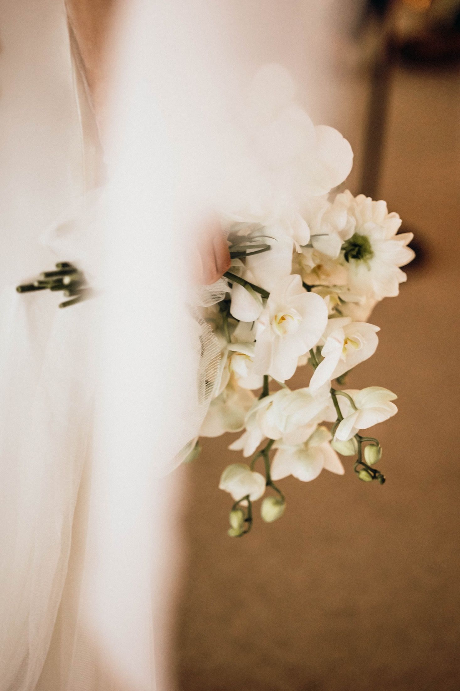 White orchids on a delicate veil create an elegant bridal detail against a soft brown background.