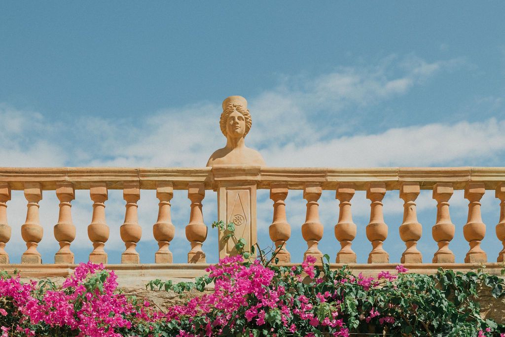 Stone balustrade with bright pink bougainvillea flowers against a blue sky.