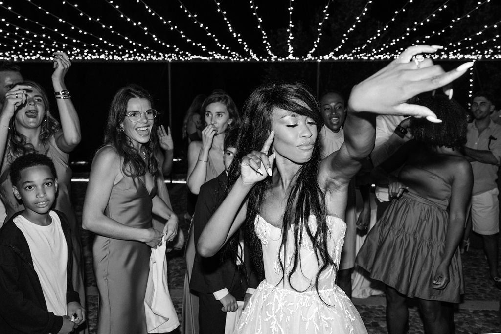 Wedding guests dancing and celebrating under string lights at an outdoor reception.