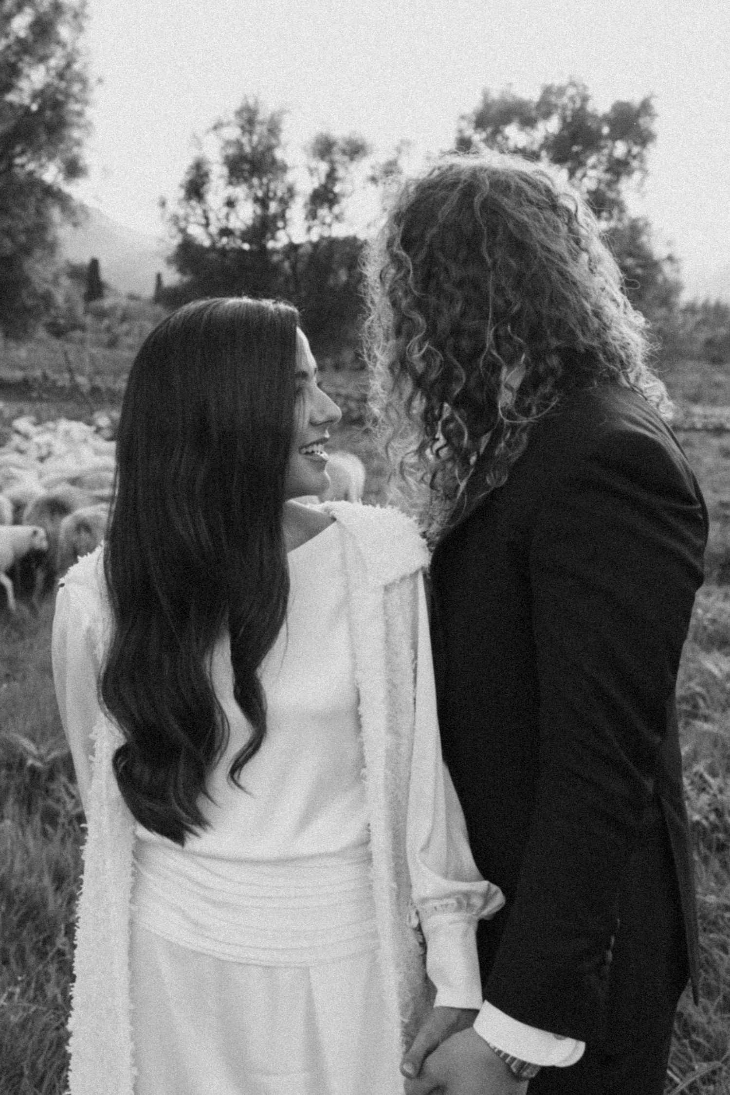 A black and white portrait showing an intimate moment between two people in a pastoral setting.