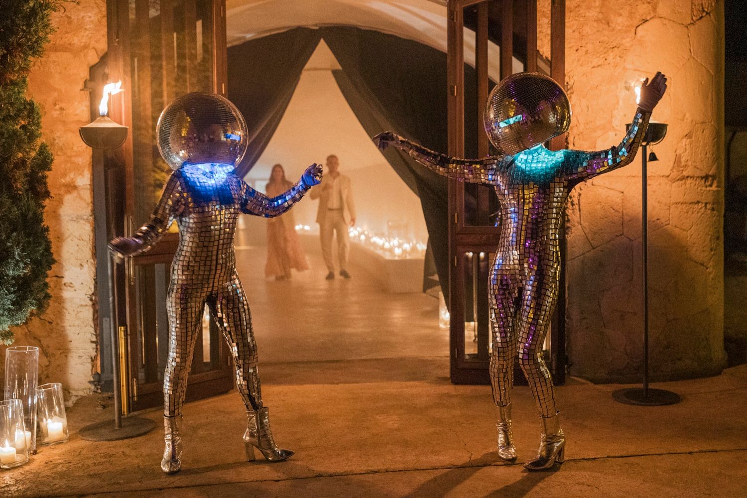 Two performers in silver sequin suits and glowing disco ball helmets pose at a glamorous event entrance.