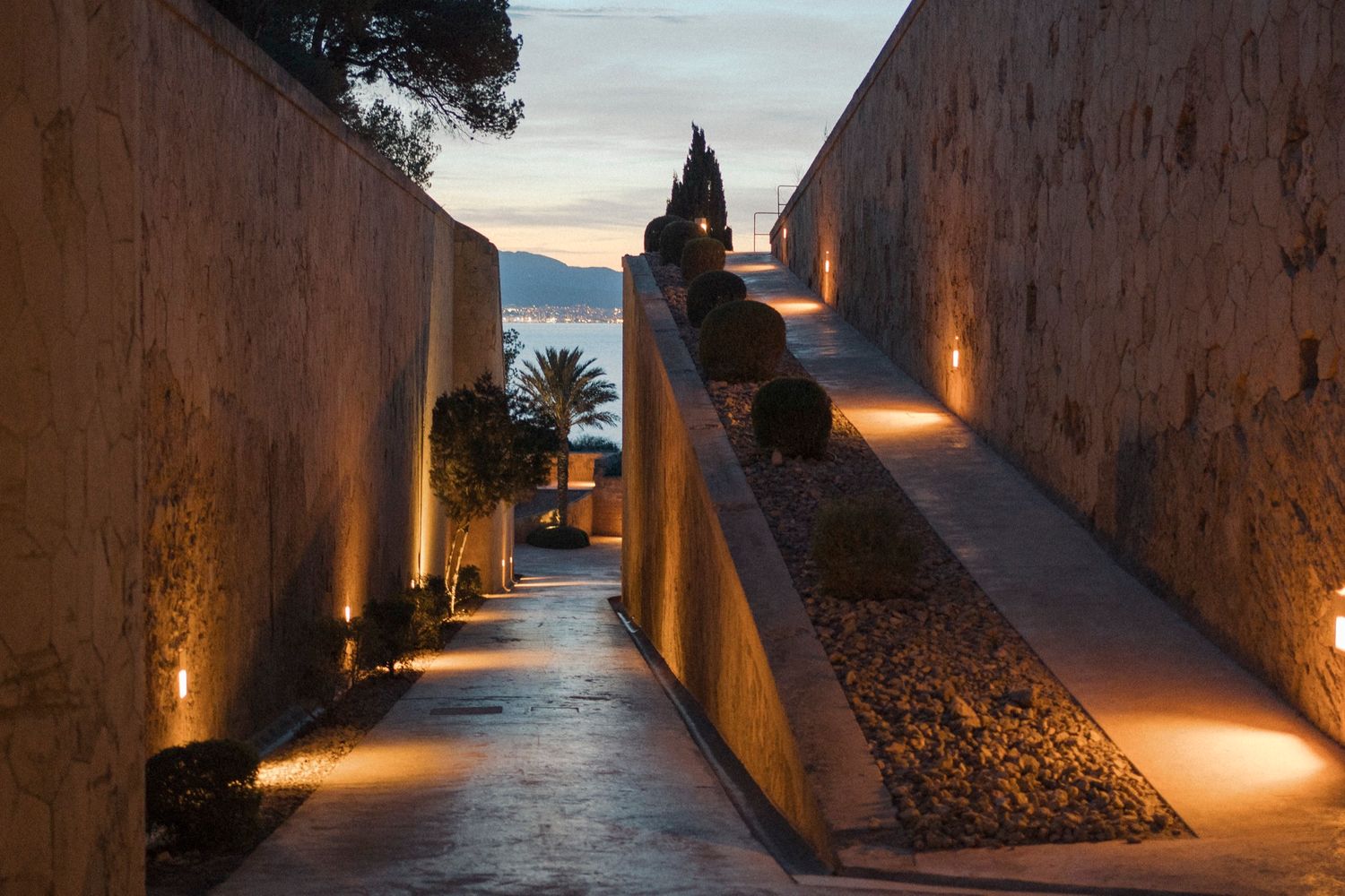 Illuminated stone pathway with warm lights and potted plants at dusk.