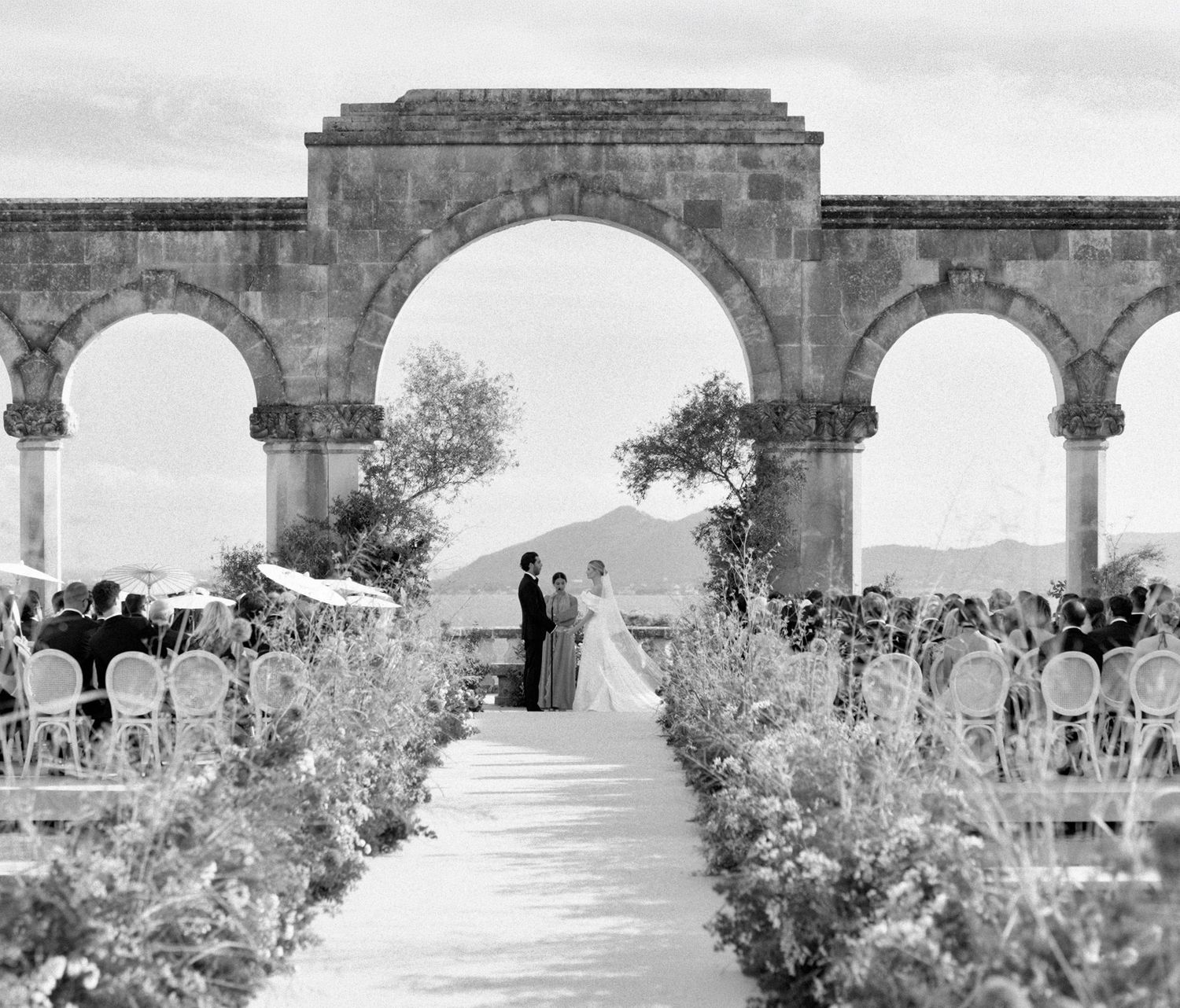 A series of stone arches in a garden setting create a scenic walkway with lush vegetation and natural lighting.