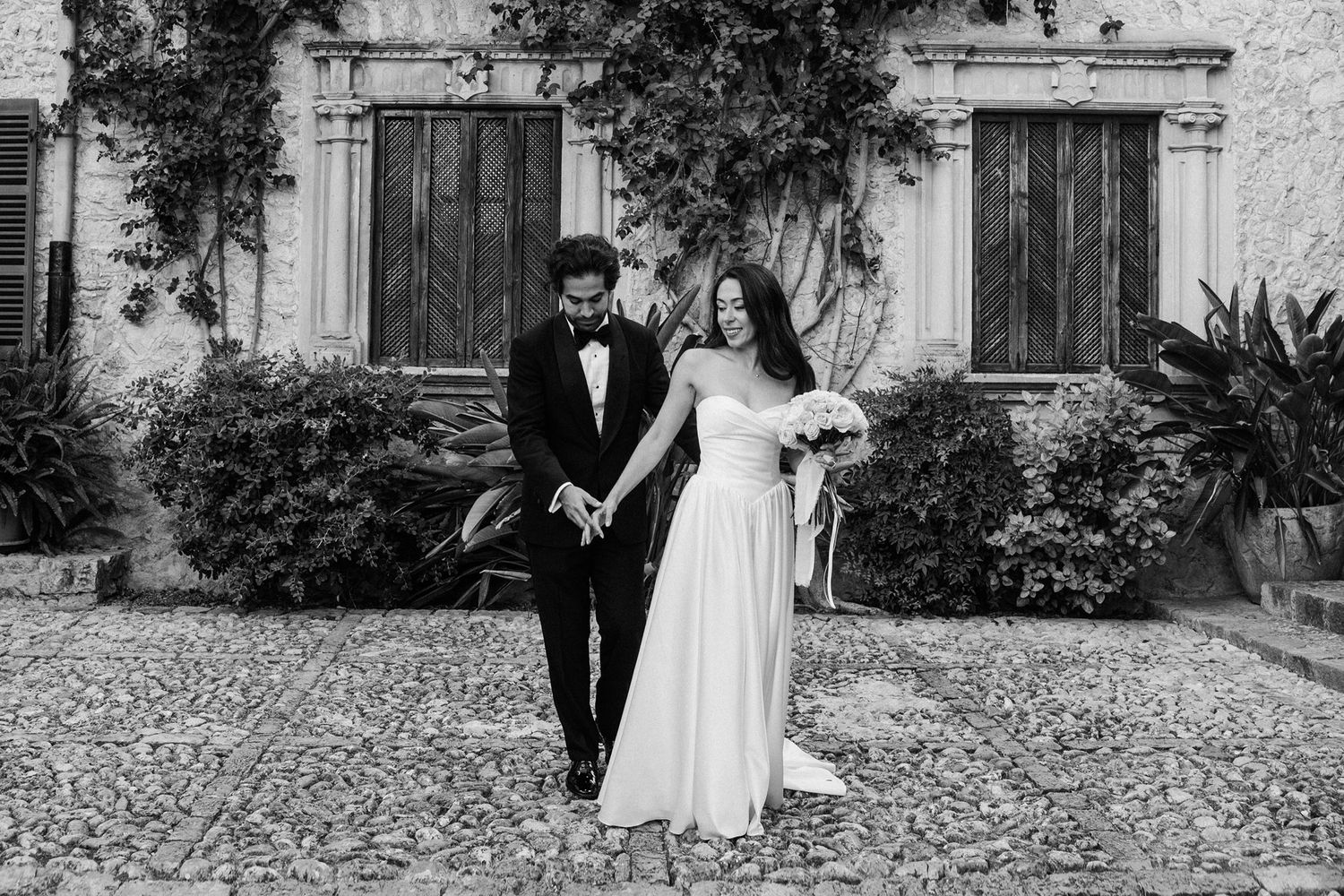 A black and white wedding photo sequence showing a couple walking and embracing on a cobblestone path. Son Berga