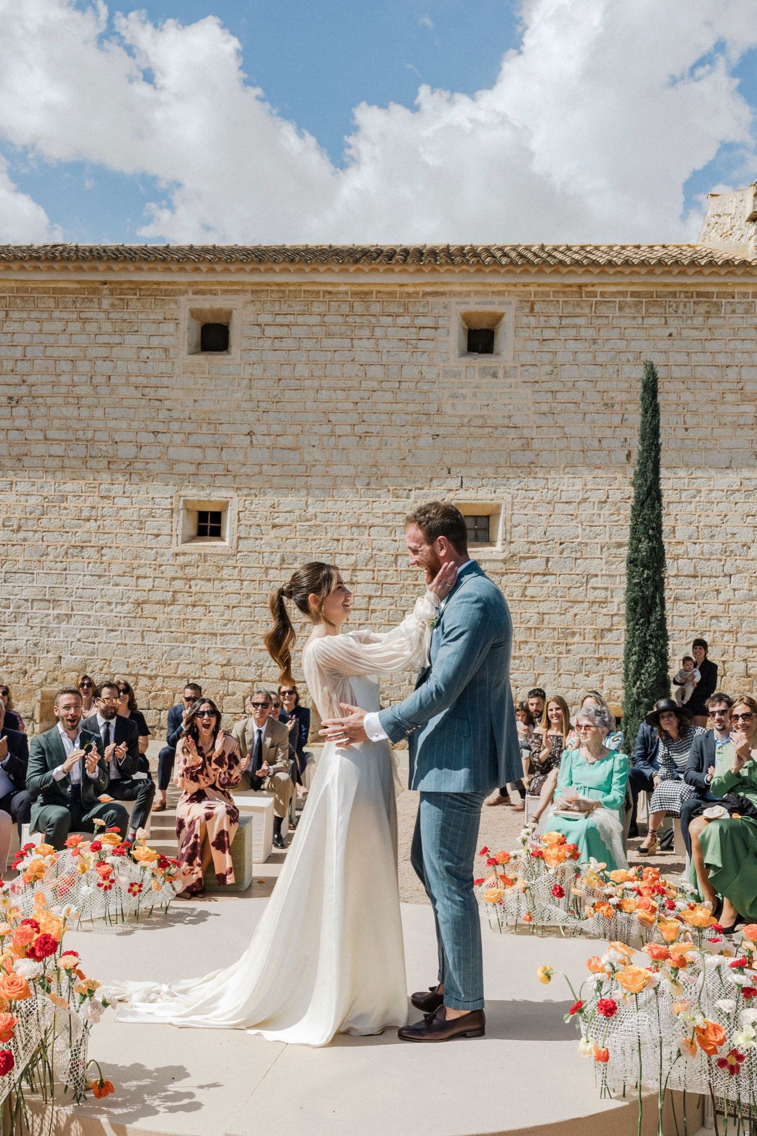 Outdoor wedding ceremony with white stone wall backdrop and colorful orange poppies lining the aisle.