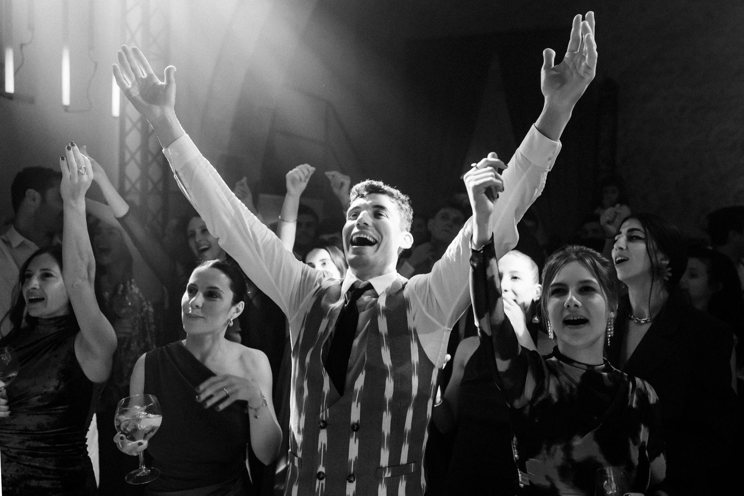 A group of people raise their hands in worship at a church service, captured in black and white photography.