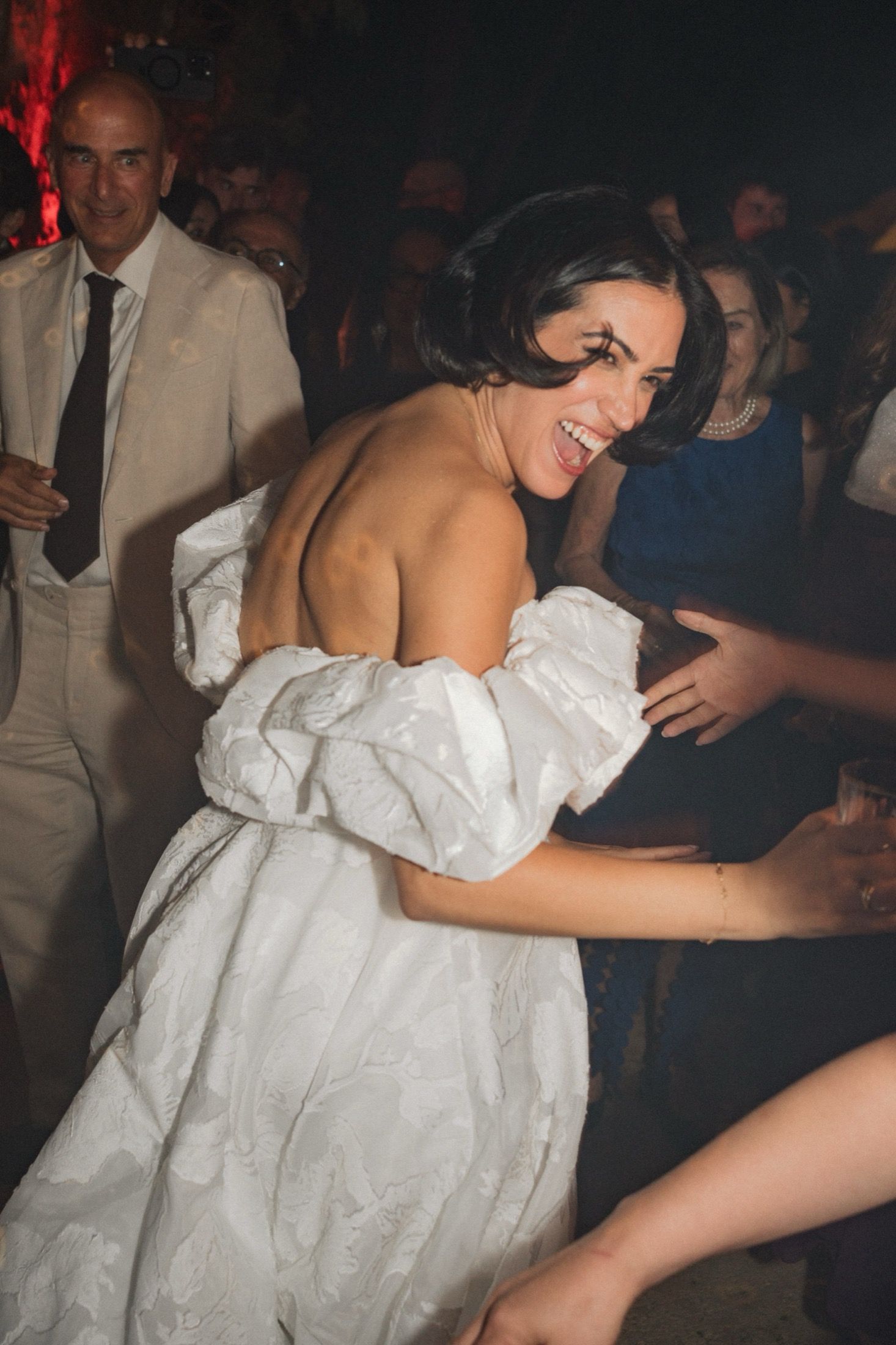 A bride in a white wedding dress dances and shows off her garter at a wedding reception.