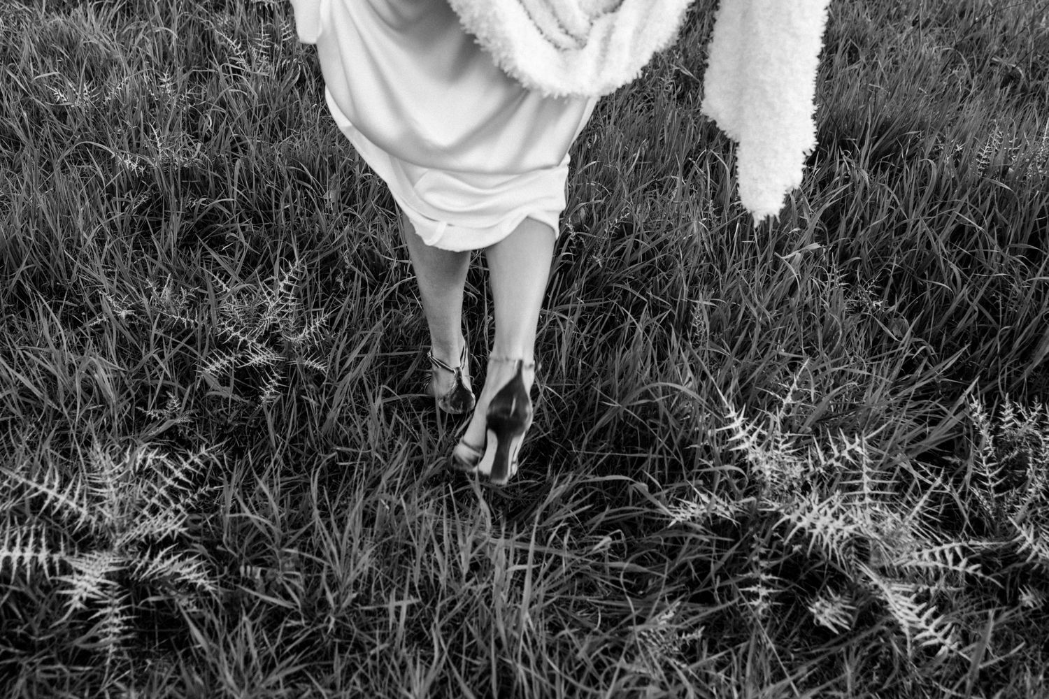 Black and white photo showing the flowing movement of a white dress in tall grass.