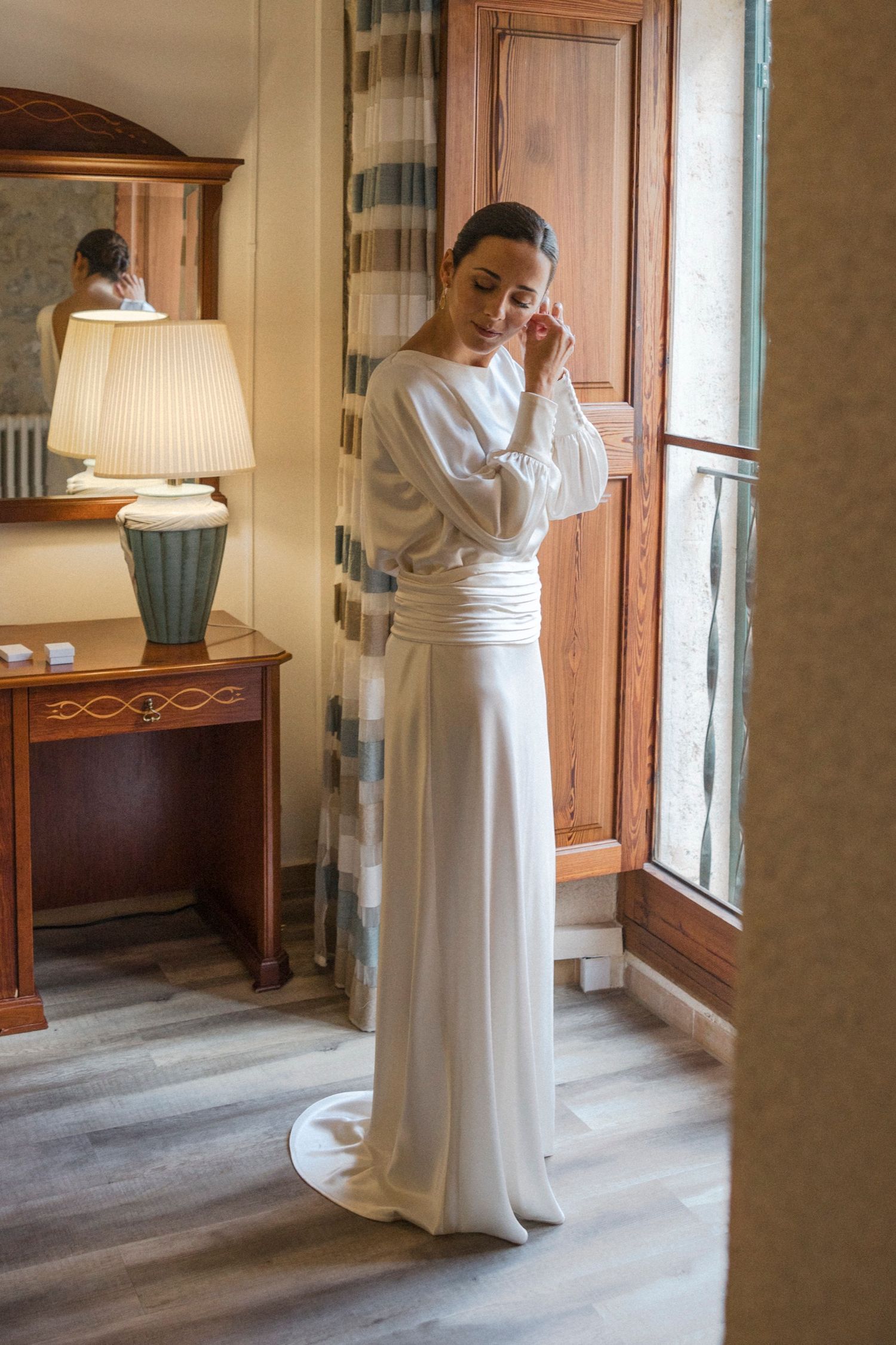 An elegant white wedding gown is showcased in a room with warm wooden accents and natural lighting.