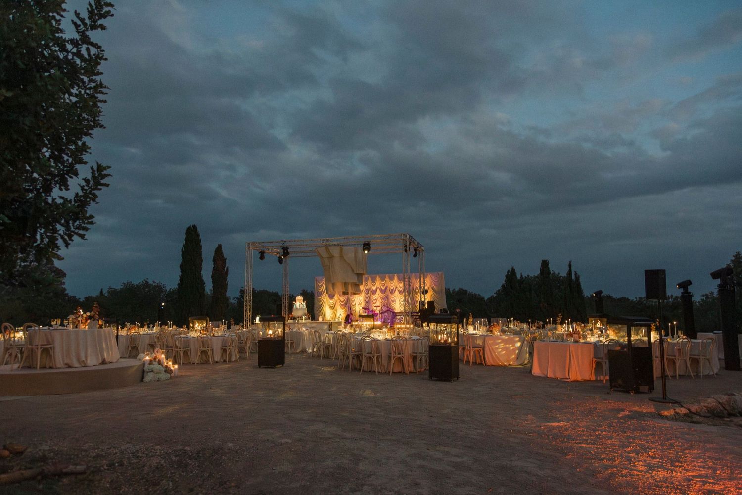 A panoramic view of illuminated adobe buildings at dusk with glowing luminarias creating a warm desert ambiance.
