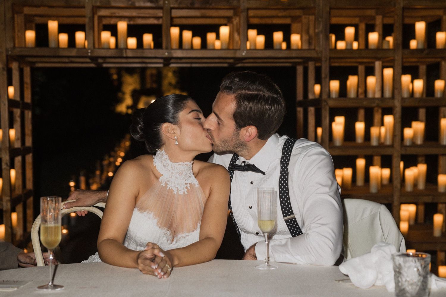 Romantic wedding couple shares intimate moments in front of glowing wall of candles at elegant reception venue.