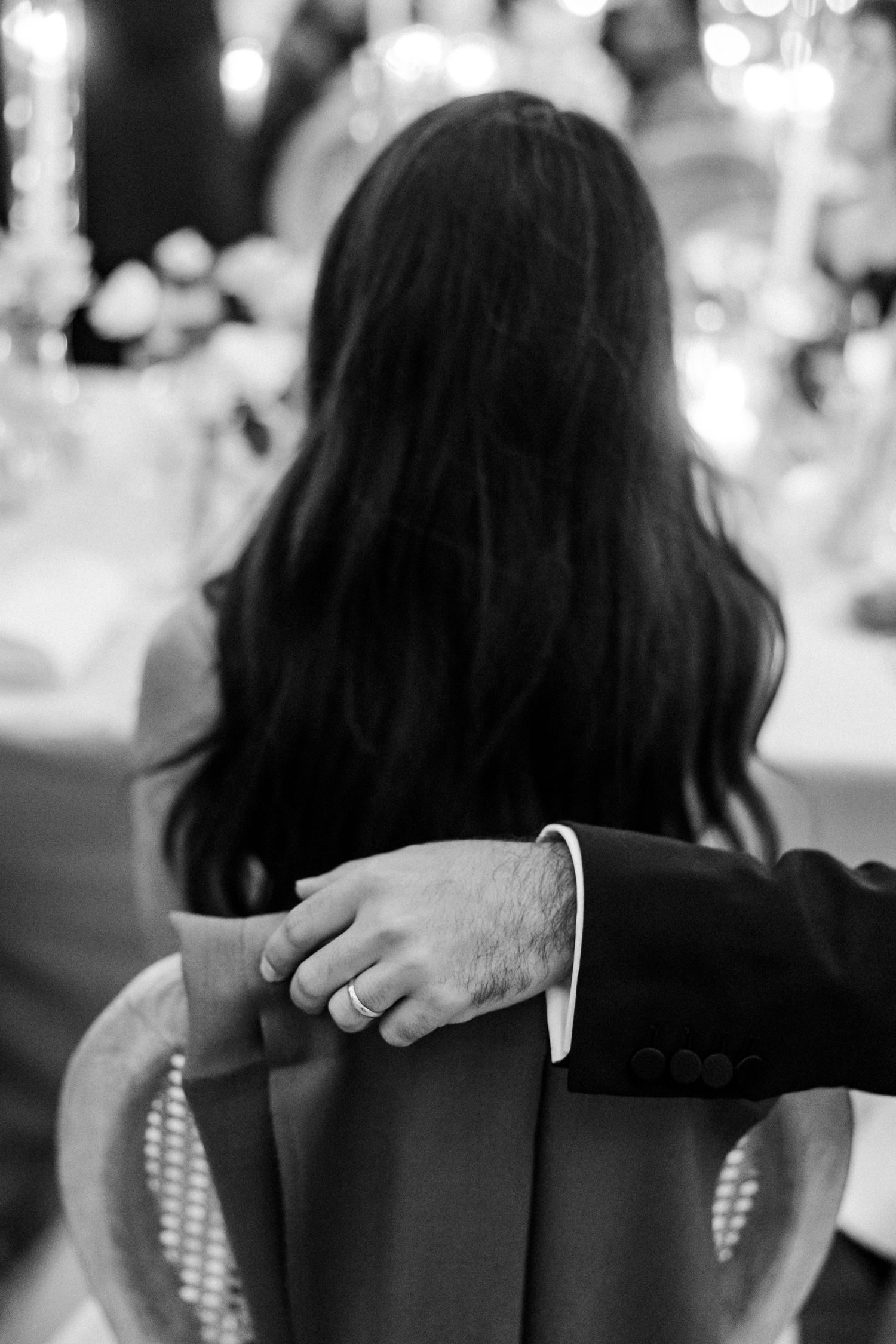 Black and white photo showing a couple's intimate moment with hands clasped during what appears to be a wedding reception.