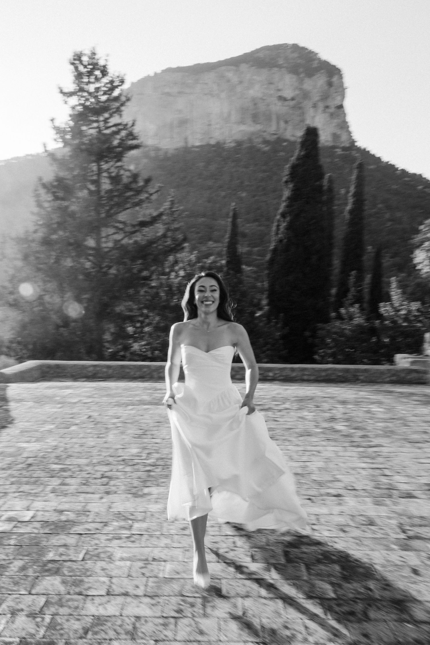 A figure in a flowing white dress dances gracefully across a stone patio with mountains and trees in the background.
